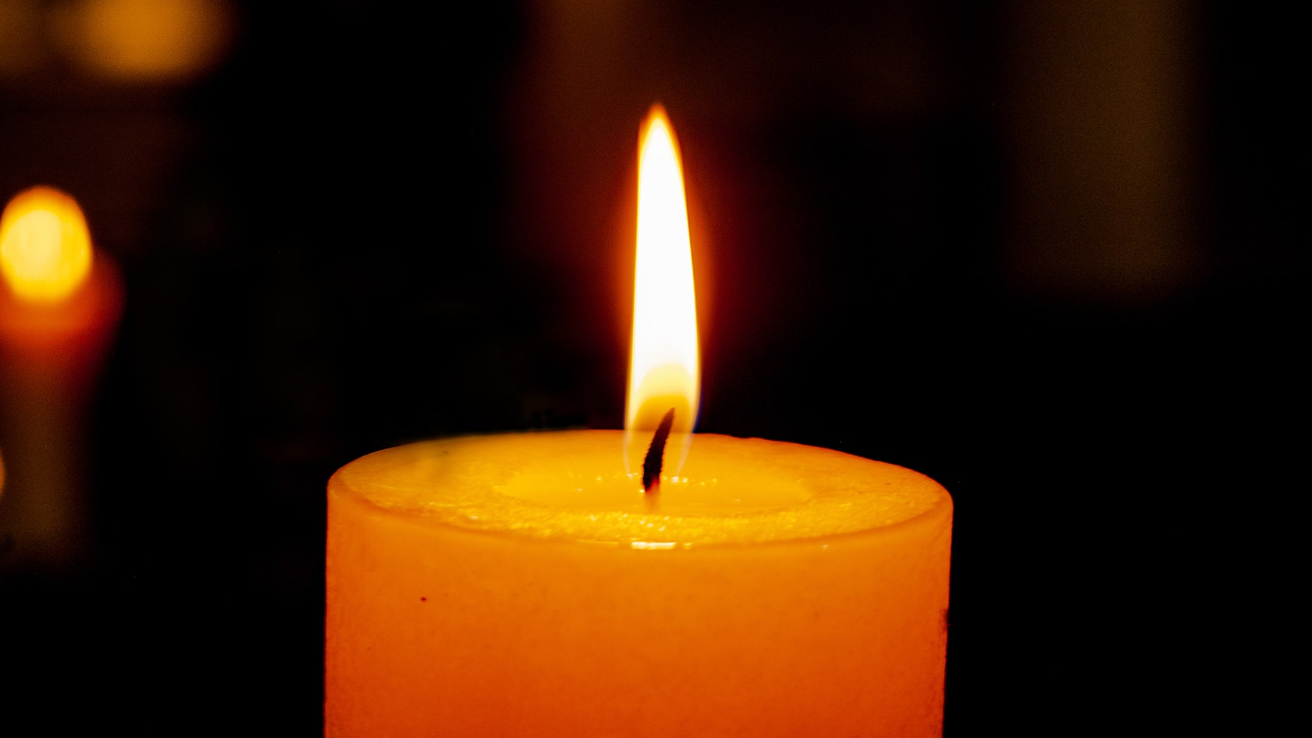 single burning candle on a dark background with reflection