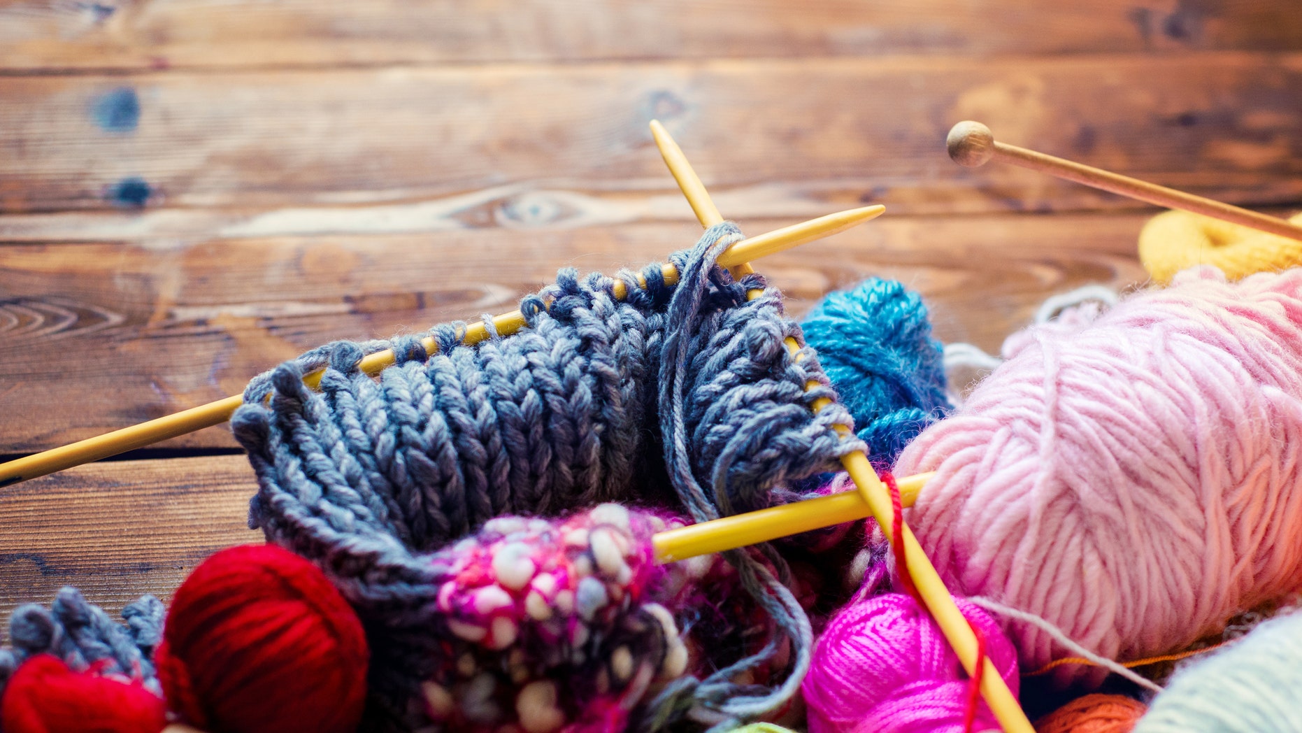 view from above on a wooden table with lots of balls of wool, knitting needles and other tools. Place for text and the word craft