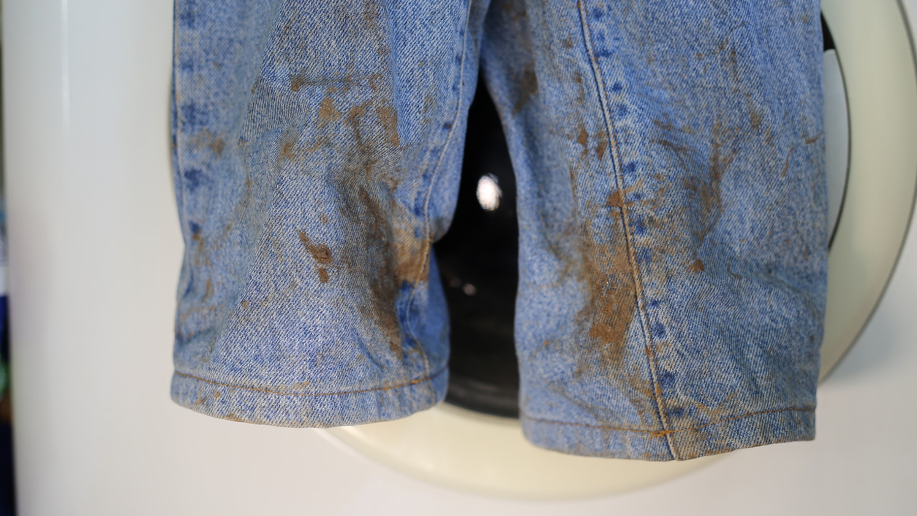 Muddy jeans on a washing machine. Mud stain on jeans. Stained jeans before laundry.