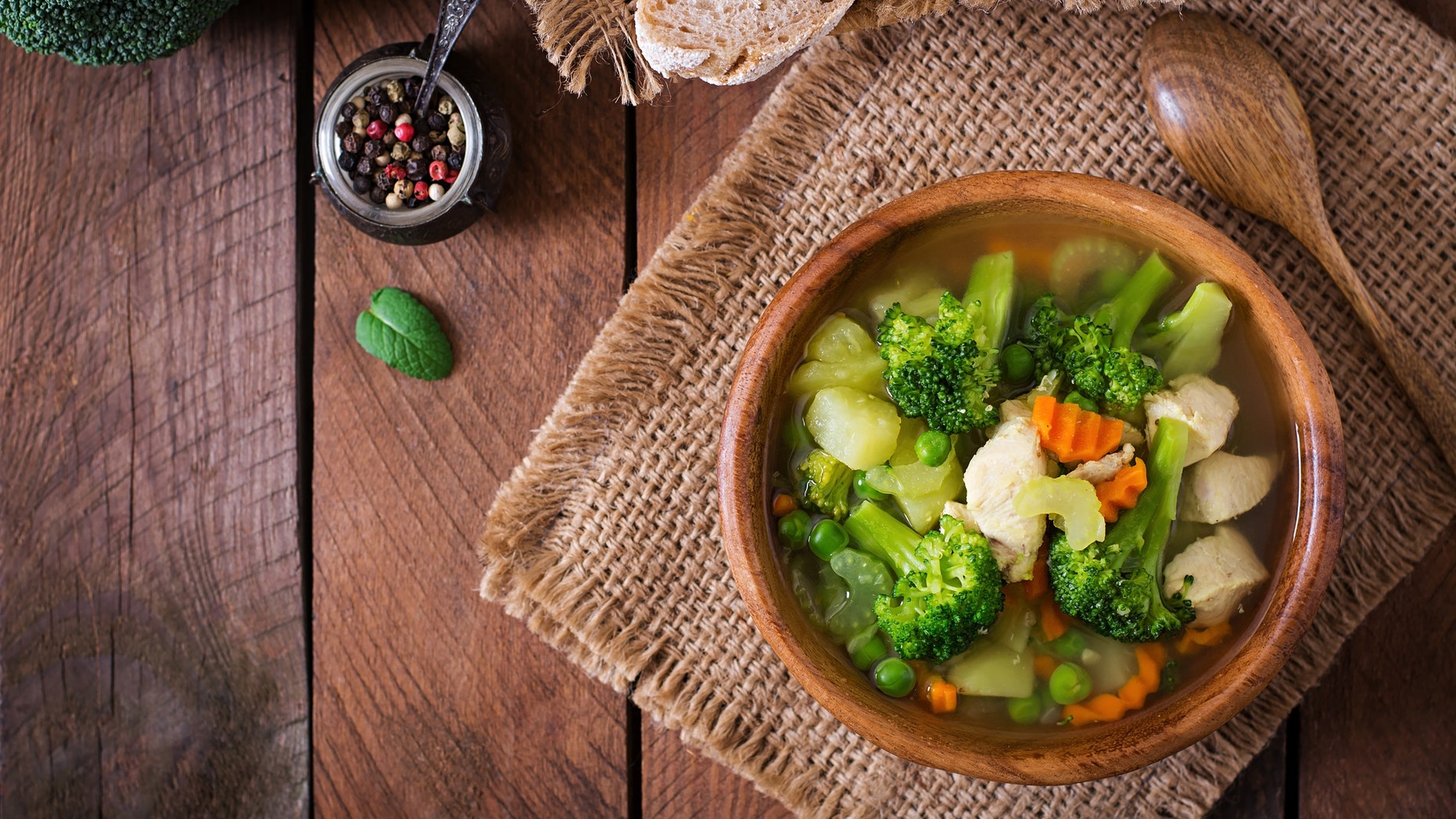 Chicken soup with broccoli, green peas, carrots and celery in bowl on a wooden background in rustic style. Top view