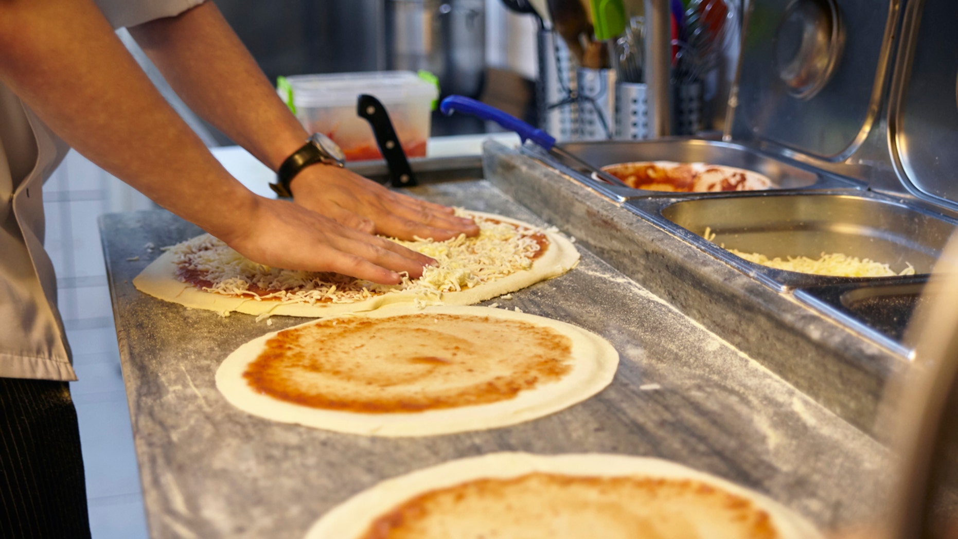 Closeup hand of chef making pizza at kitchenCloseup hand of chef adding parmesan on pizza