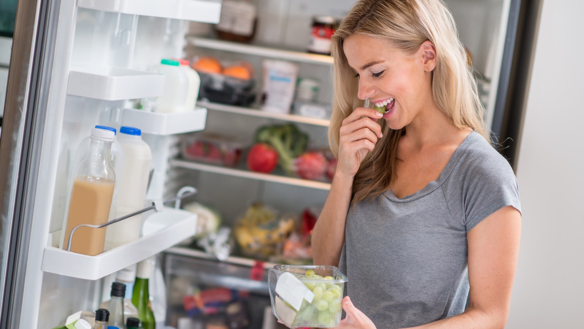 Healthy eating woman at the fridge eating grapes