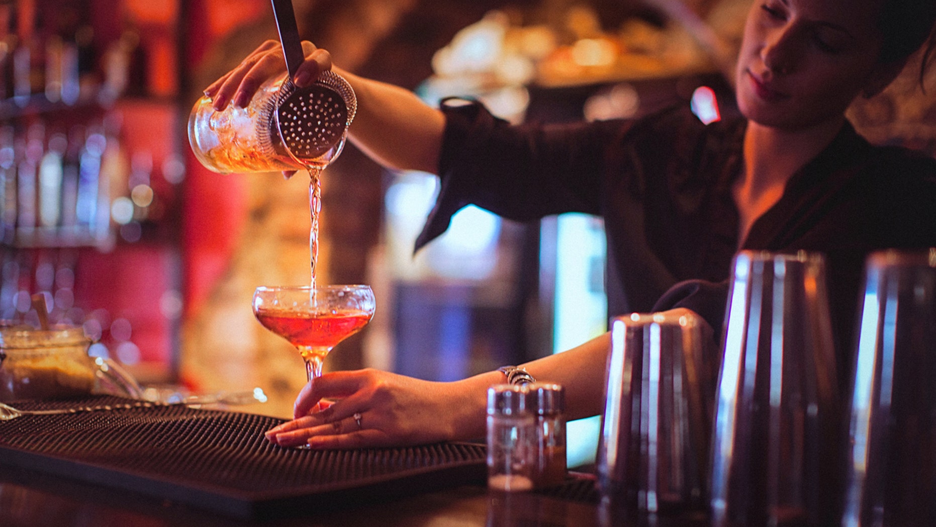 Close-up of a young female bartender pouring cocktail in a nightlife cocktail bar. Selective focus. Focus on foreground.