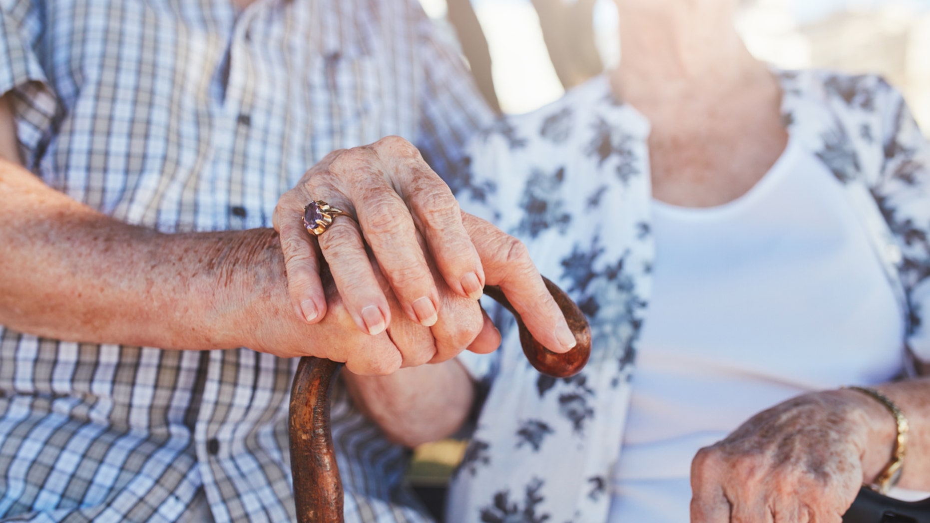 Cropped shot of senior couple holding hands while sitting together. Focus on hands on walking stick.