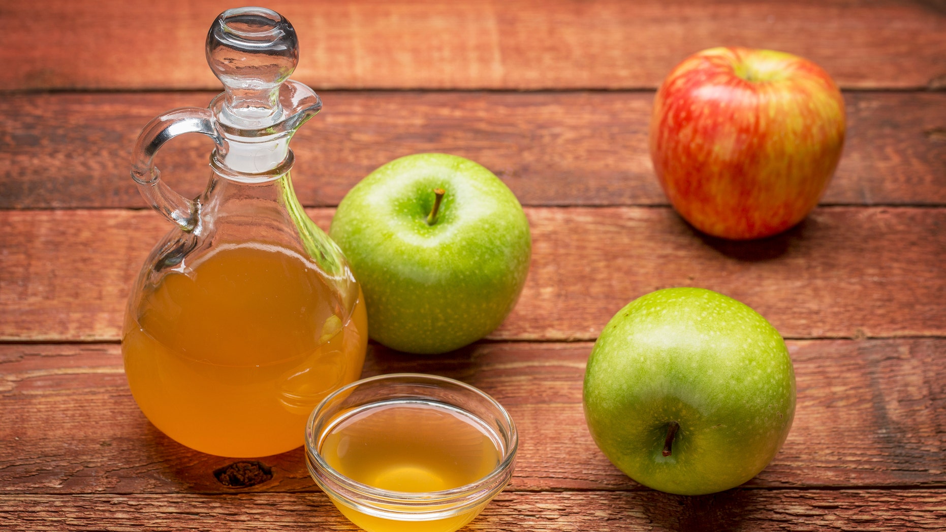 unfiltered, raw apple cider vinegar with mother - a cruet with a small glass bowl surrounded by fresh apples on rustic wood