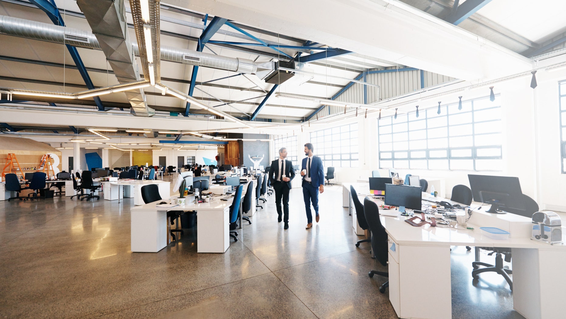 Shot of two colleagues walking and talking during a coffee break at work