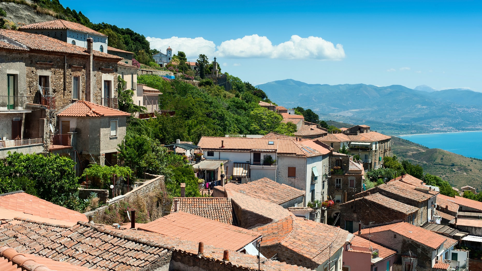 Roofs of old buildings on the hill with sea and mountains on background. This picture was taken in Acciaroli, Cilento park area, Campania, Italy.