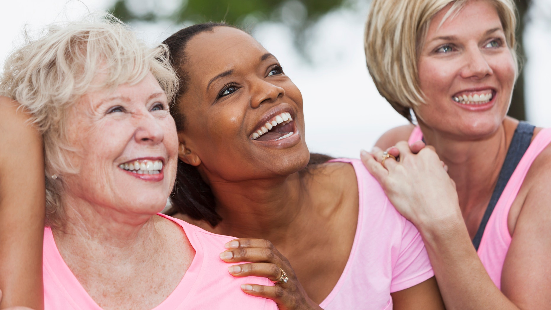 Multi-ethnic women (40s, 60s) wearing pink, participating in breast cancer rally. Main focus on African American woman (40s) standing in middle.