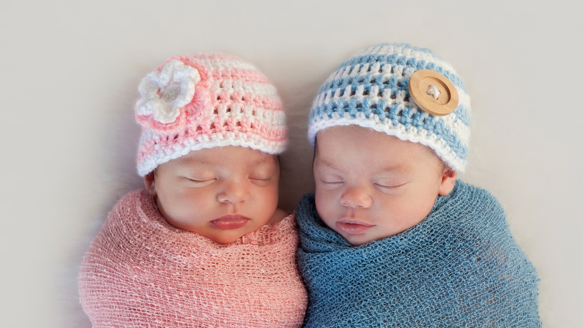 Five week old sleeping boy and girl fraternal twin newborn babies. They are wearing crocheted pink and blue striped hats.
