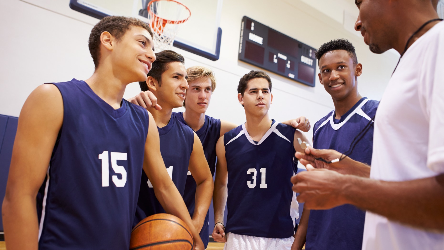 Male High School Basketball Team Having Team Talk With Coach In Gymnasium