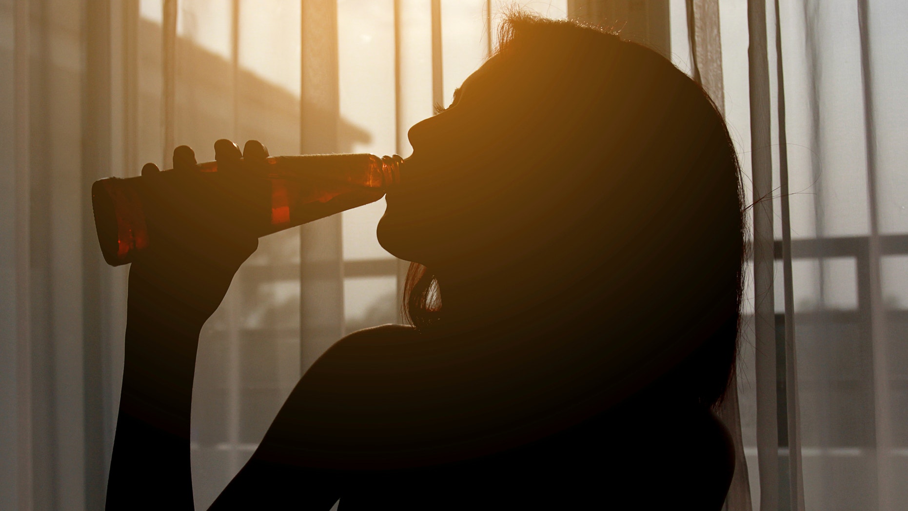Silhouette shot of a female drinking red wine in a room