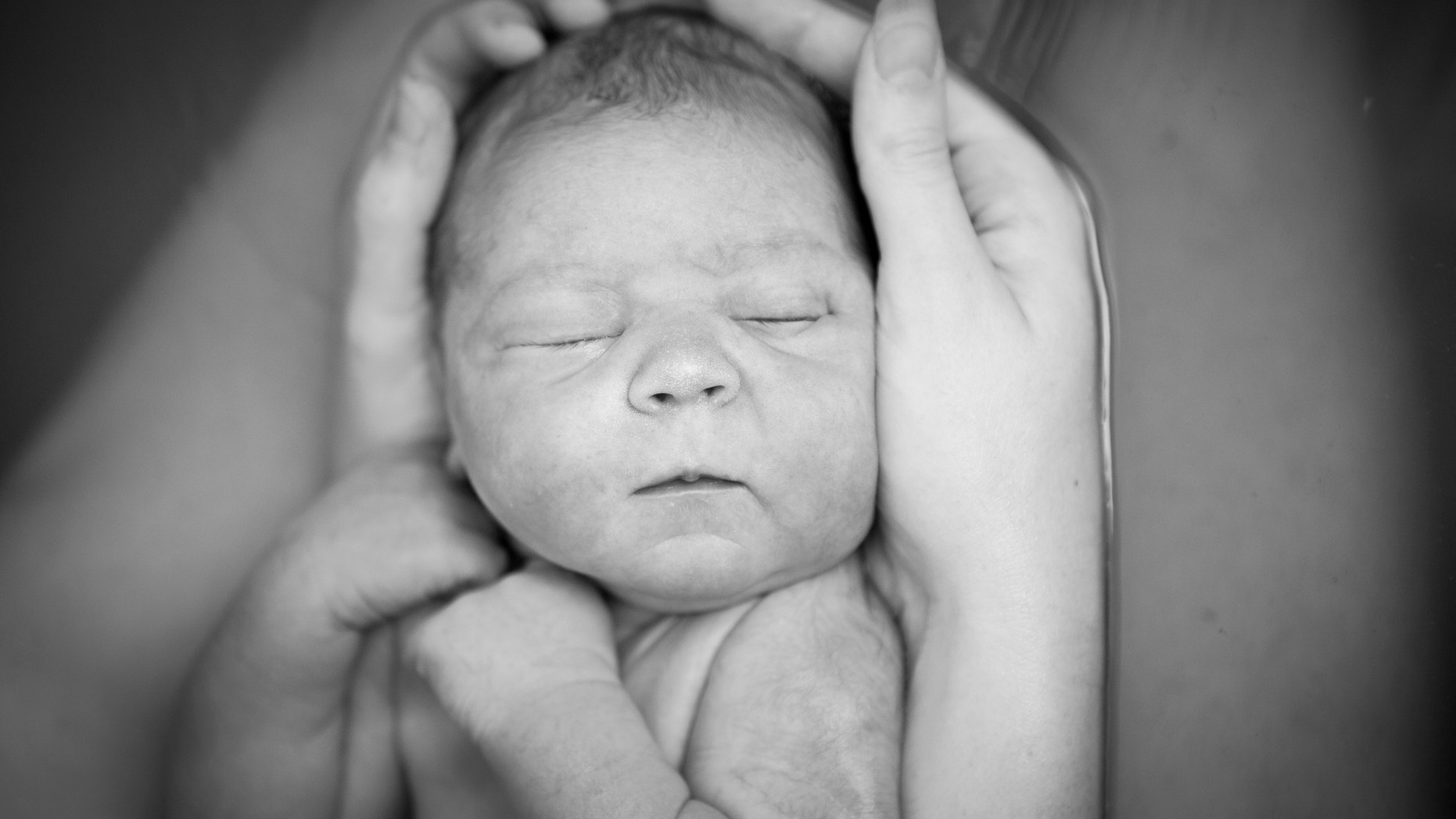 Black and white image of a young mother holding her newborn son after giving birth at home.
