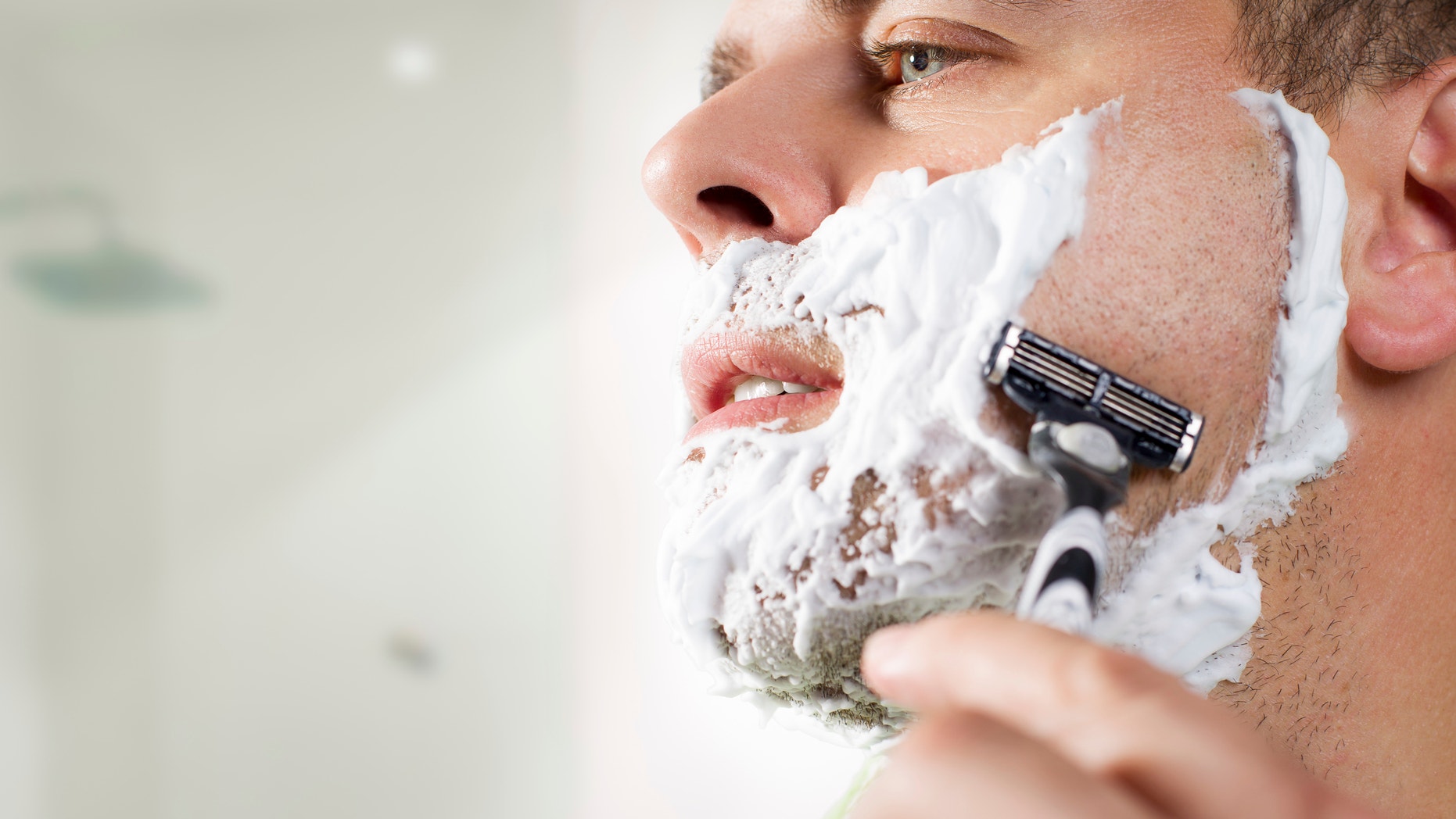 Happy middle aged man using razor to shave