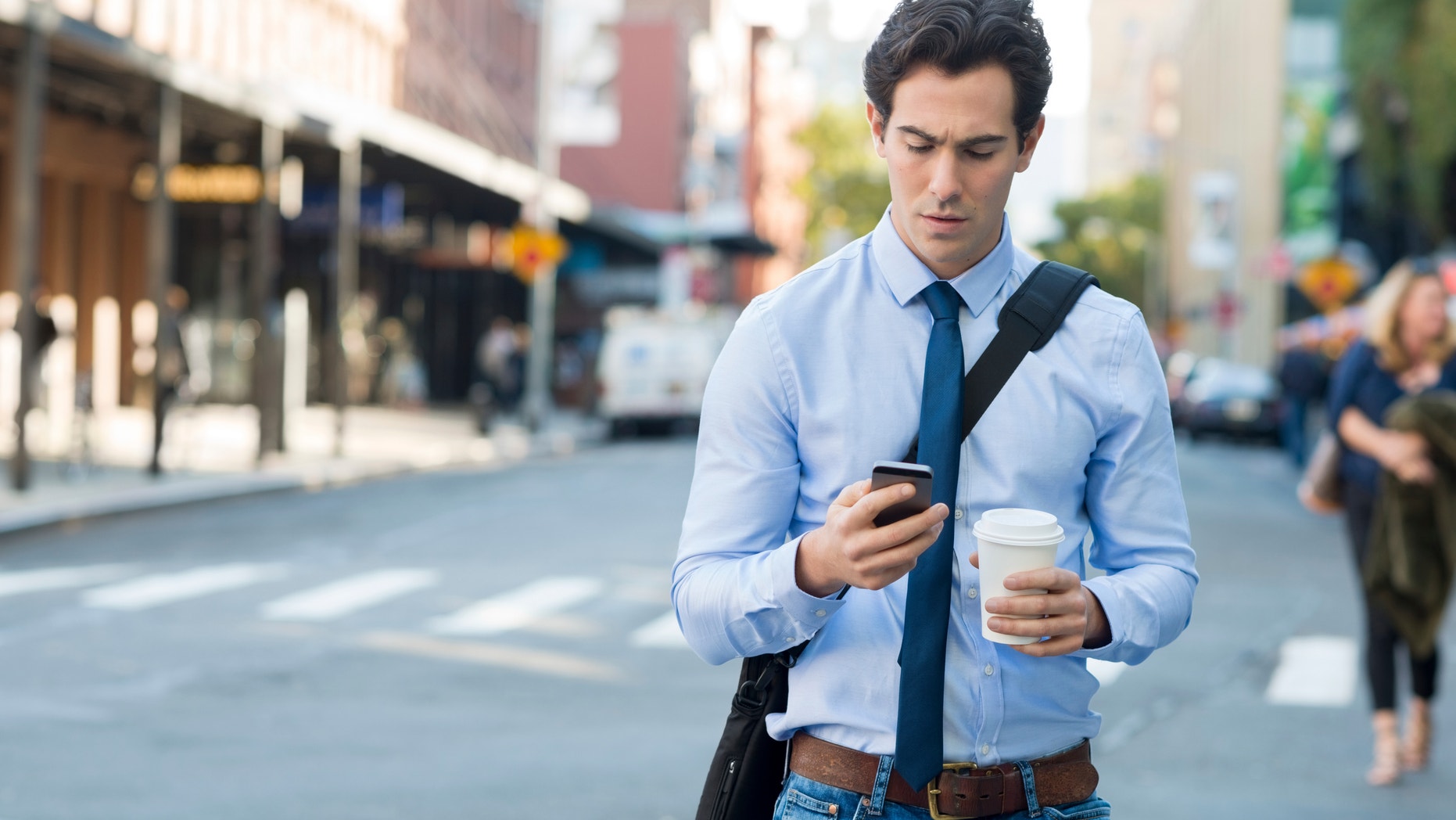 Businessman using smartphone and holding paper cup in an urban scene.