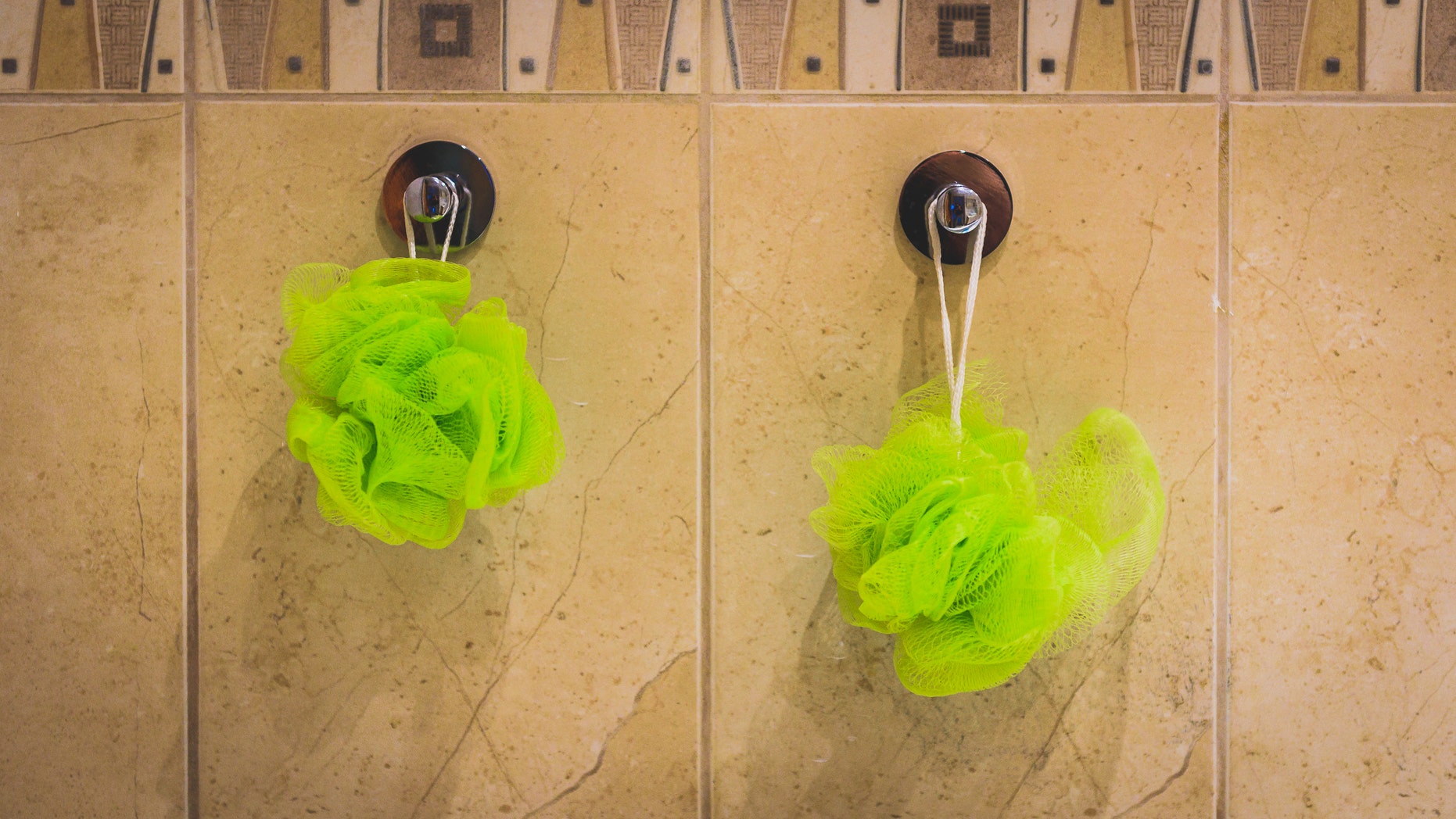 Two green bath sponges hanging from the bathroom wall. Bath accessories hanging from bathroom tiles.