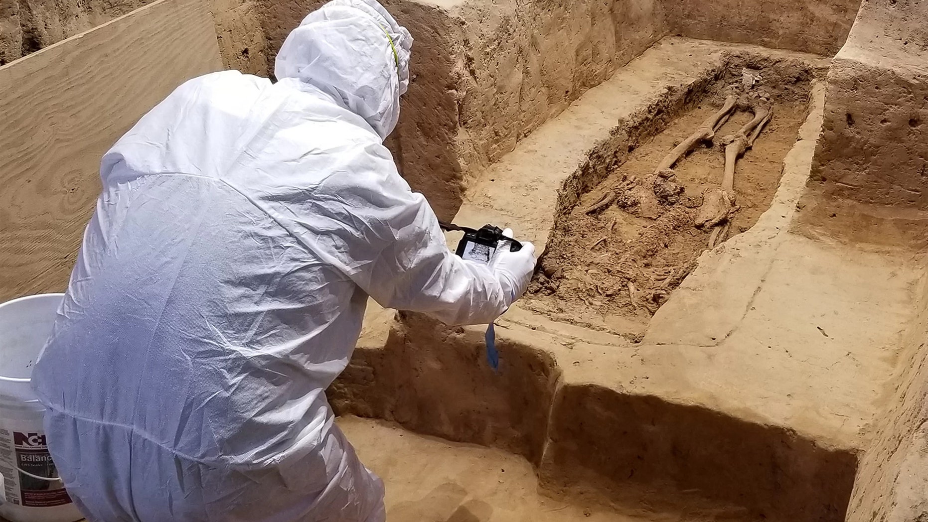 An archaeologist investigates the burial while wearing a suit that will minimize contamination to the historical site. Credit: Jamestown Rediscovery