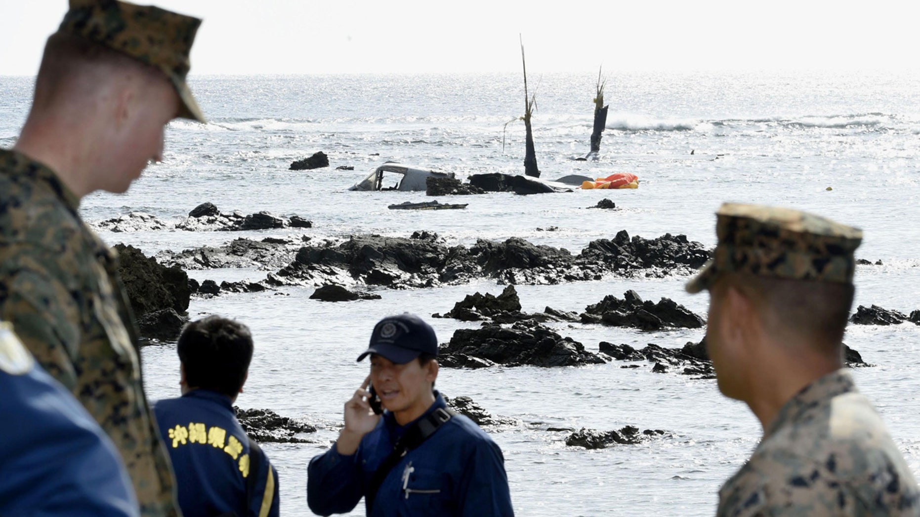 Officers of Okinawa Prefectural Police and the U.S. military investigate the site where debris of the MV-22 Osprey, background, was spotted in shallow waters off Okinawa.