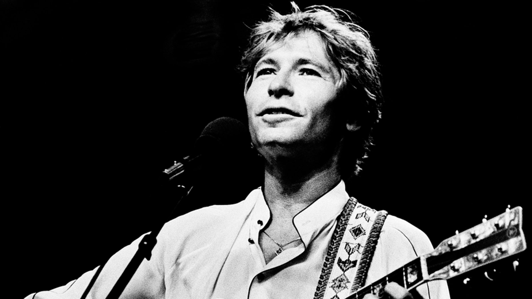 July 28, 1983. John Denver strums his guitar as he performs during an outdoor concert on the Boston Common, Boston, Mass.