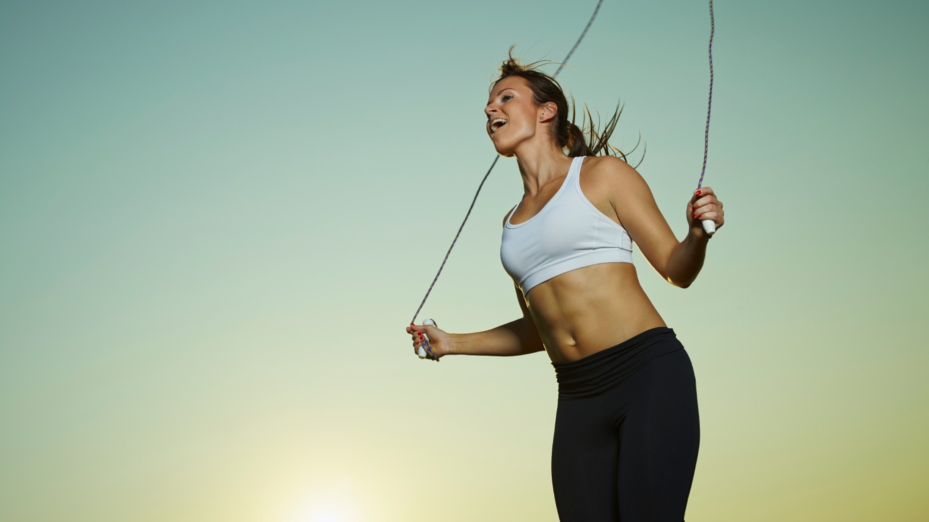Young fitness woman used a skipping rope, sun and sky on background, copy space