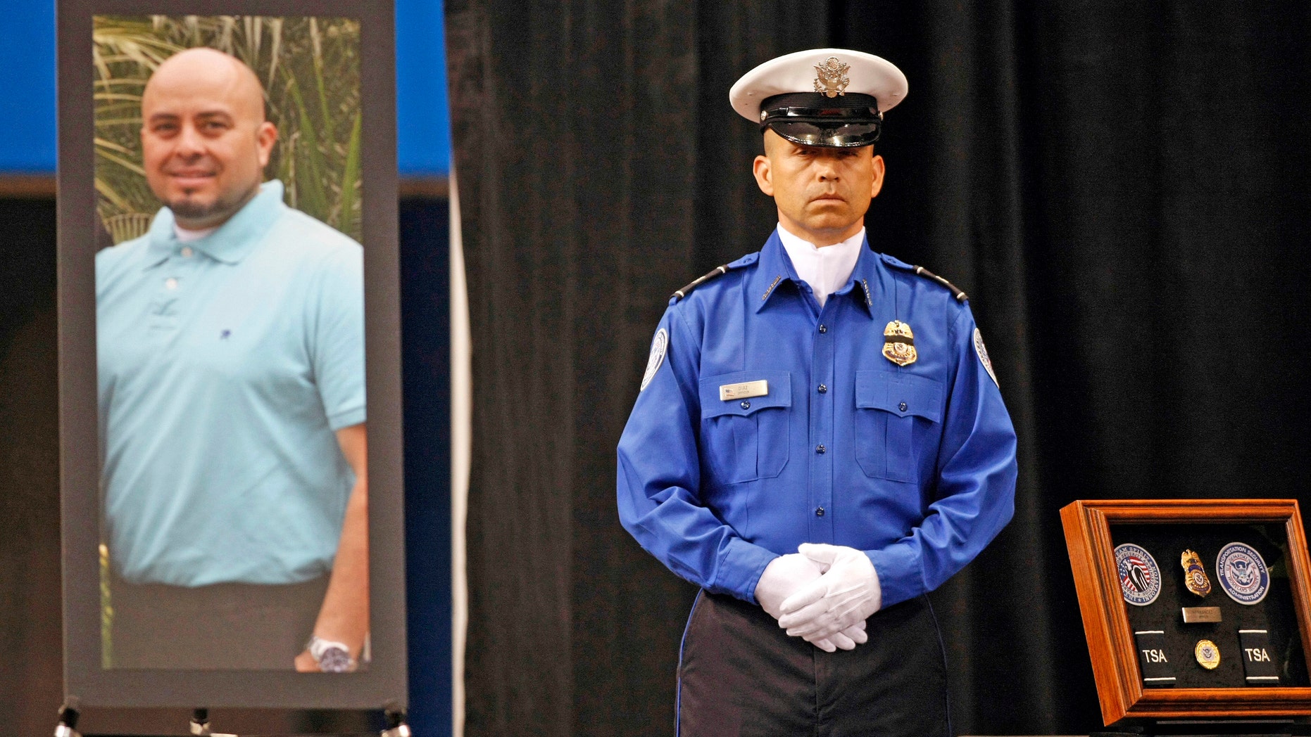 A TSA officer stands in front of a portrait of slain TSA officer Gerardo Hernandez during his public memorial at the Los Angeles Sports Arena.