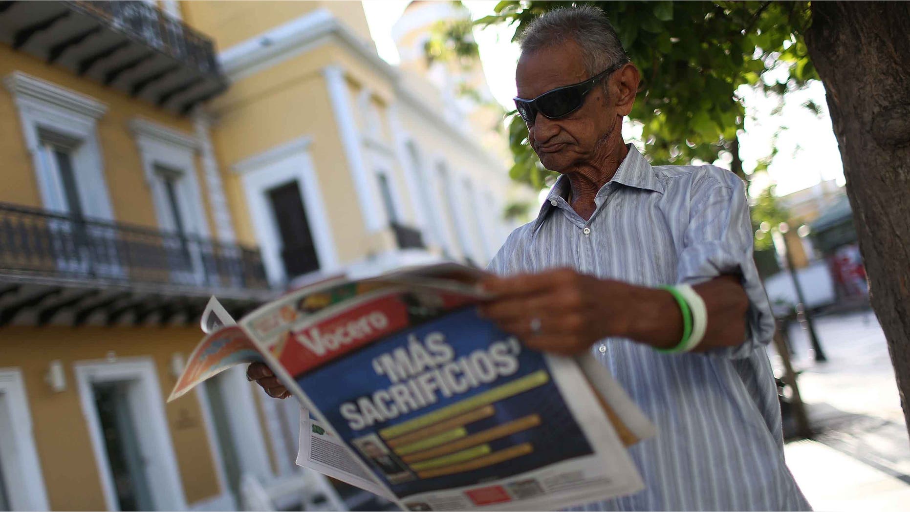Jose Vasquez reads a newspaper with a Spanish headline that reads 'More sacrifices' in San Juan, Puerto Rico.