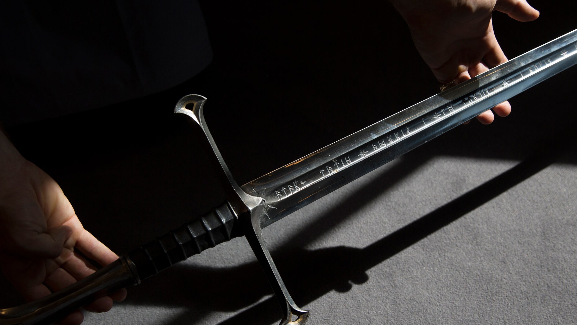 A gallery assistant poses for a photograph with a sword used in the Lord of the Rings film "Return of the King" in Bonhams auction house in London July 31, 2014. (REUTERS/Neil Hall)
