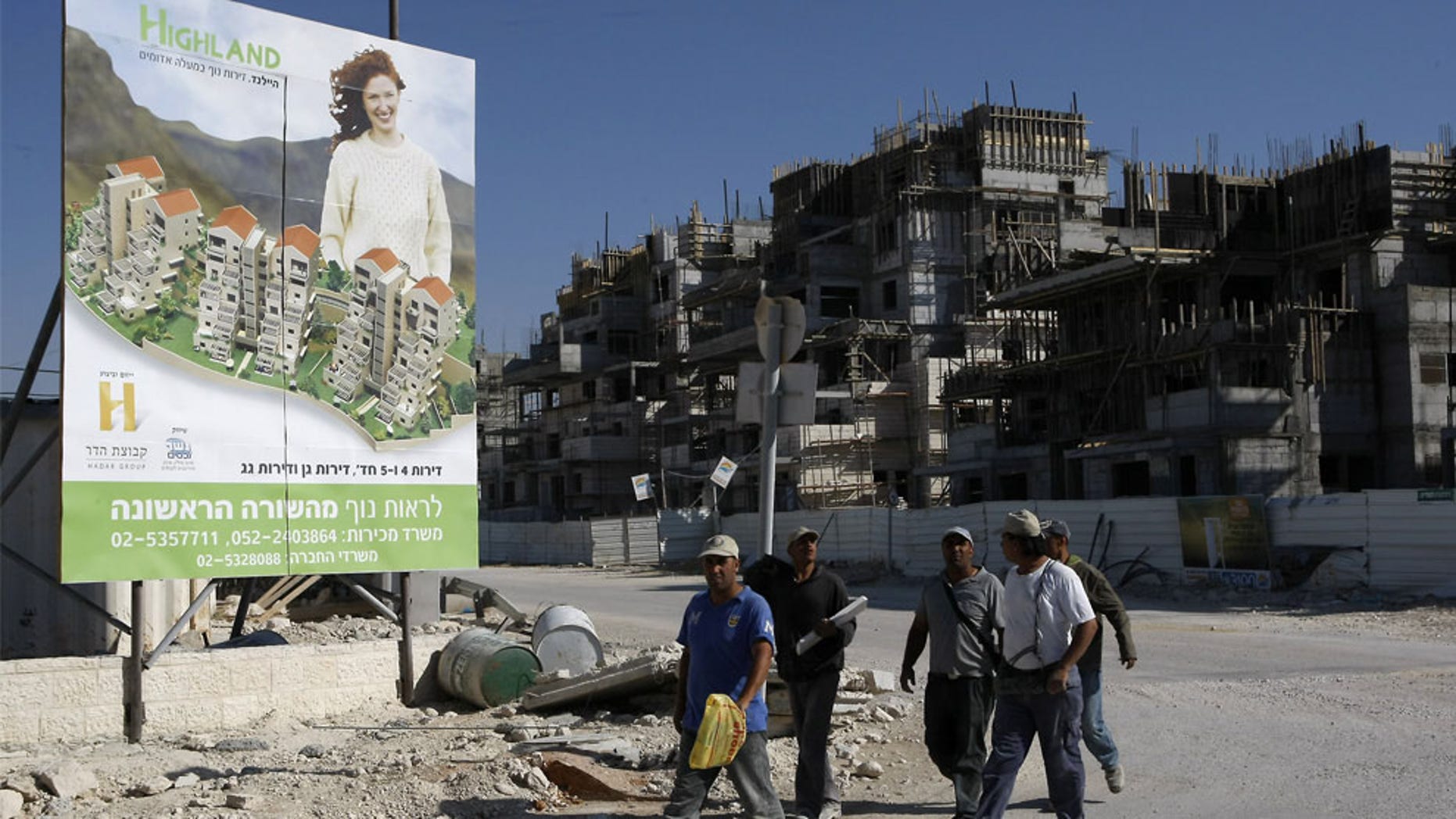 FILE: Palestinian laborers walk past a billboard advertising a new housing project in the Jewish settlement of Maale Adumim in the occupied West Bank. (AFP)