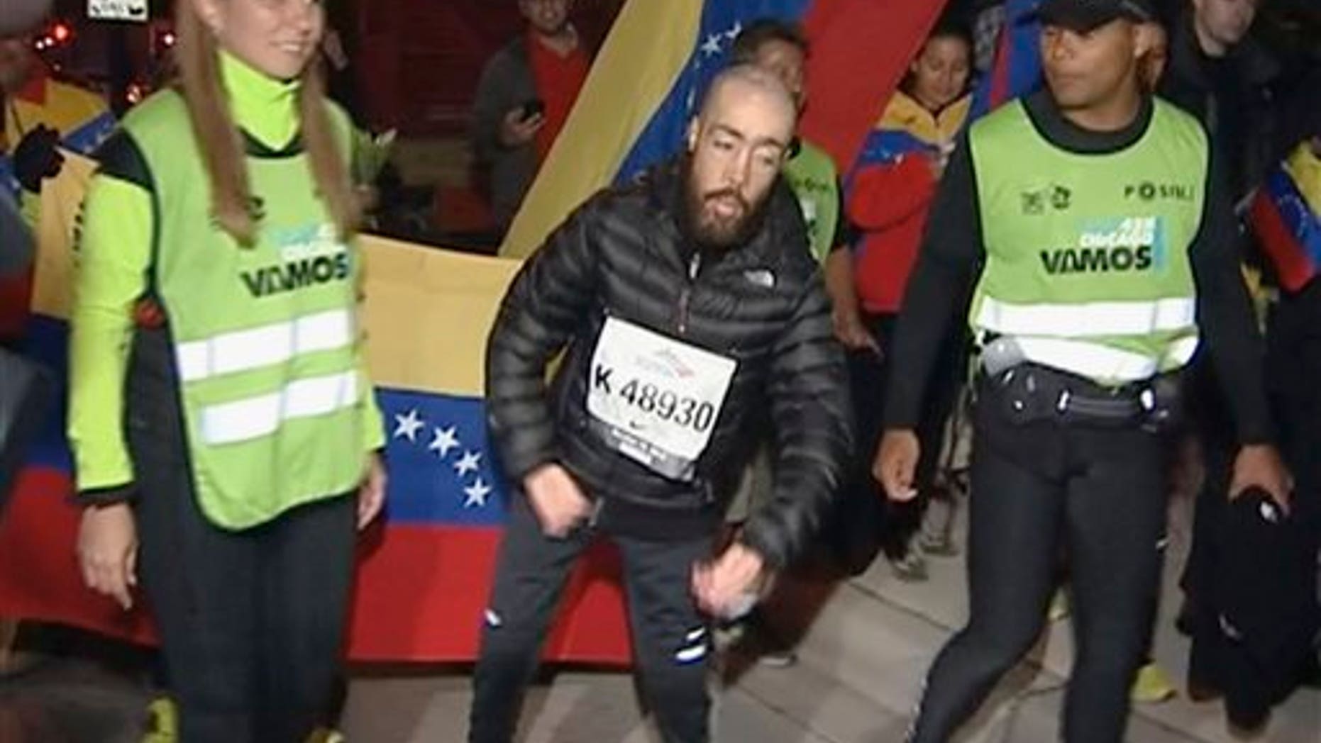 This photo from video provided by Ken Herzlich of Embargo Chicago shows Maickel Melamed, 38, center, of Venezuela, who has muscular dystrophy, nearing the finish line early Monday, Oct. 14, 2013, to be the last runner to finish the Chicago Marathon.
