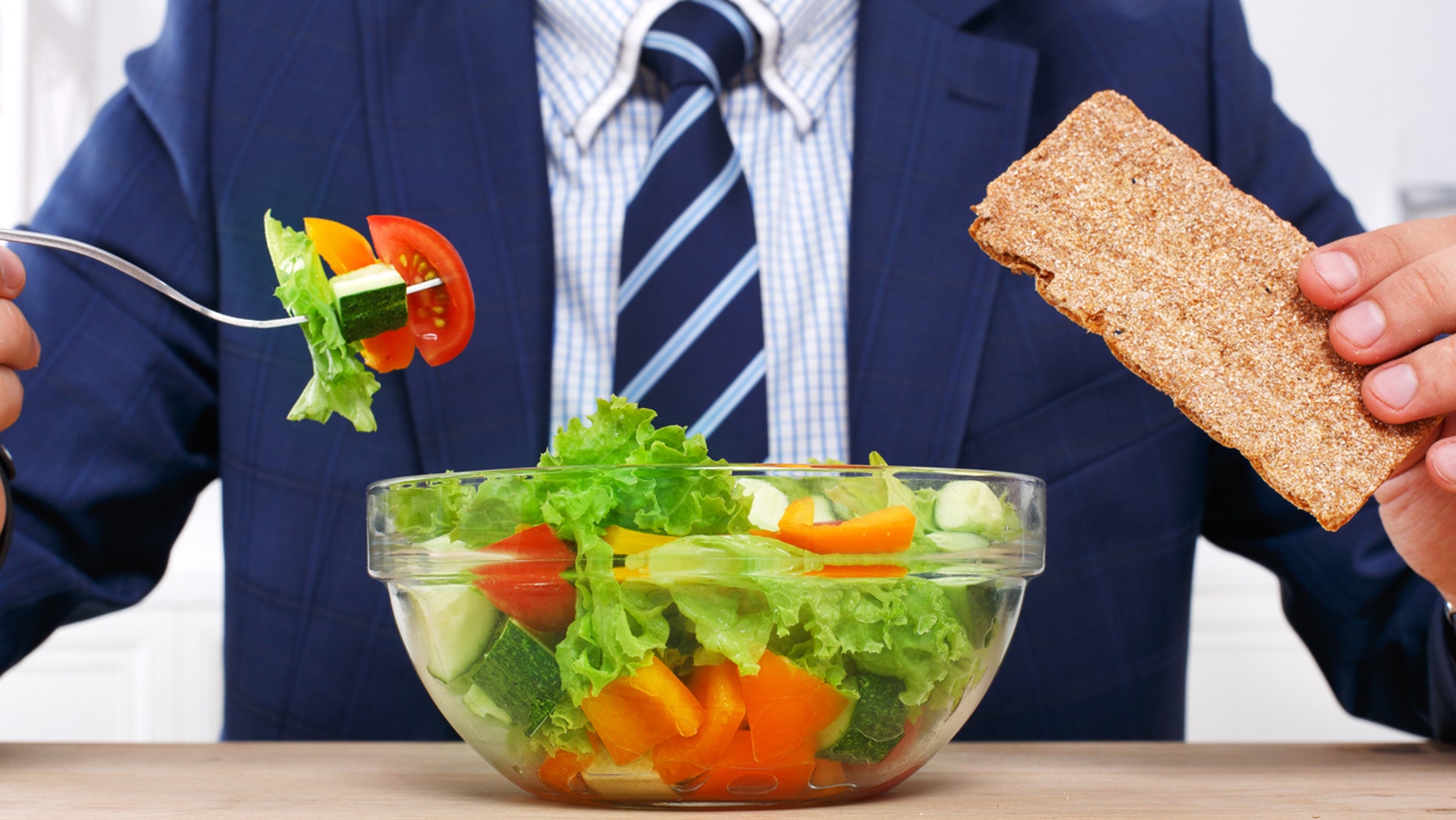 Man in suit unrecognizable torso eating healthy business lunch in modern office interior. Businessman at working place with vegetable salad in bowl, diet and right nutrition concept.