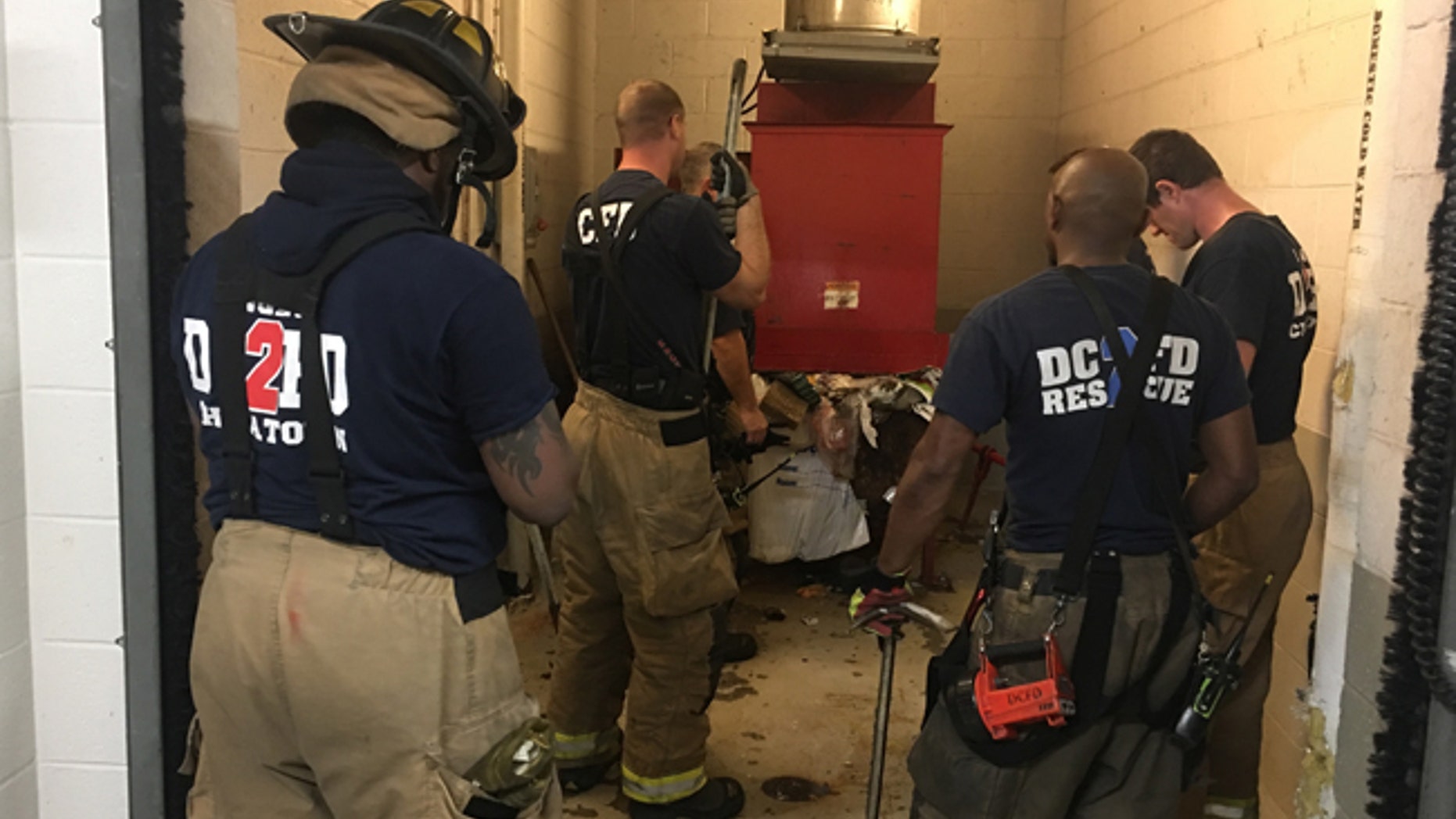 In this photo provided by DC Fire and EMS, emergency personnel respond to a call from a man who was stuck in a trash chute, early Sunday, July 23, 2017, in Washington. Spokesman Vito Maggiolo says the man was throwing out trash at the apartment building when he thought he dropped a cellphone in the chute. Maggiolo says the man leaned in to check and fell inside. (Vito Maggiolo/DC Fire and EMS Department via AP)