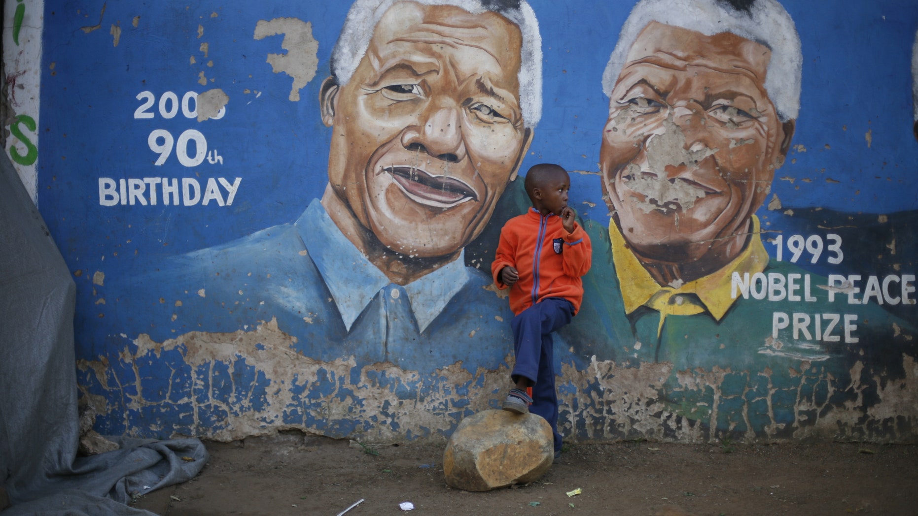 Hussein Gallo, 7, stands by a mural of Nelson Mandela in the Soweto township in Johannesburg, South Africa, Saturday June 7 2013. Former South African President Nelson Mandela is in "serious but stable" condition after being taken to a hospital to be treated for a lung infection, the government said Saturday, prompting an outpouring of concern from admirers of a man who helped to end white racist rule. (AP Photo/Jerome Delay)