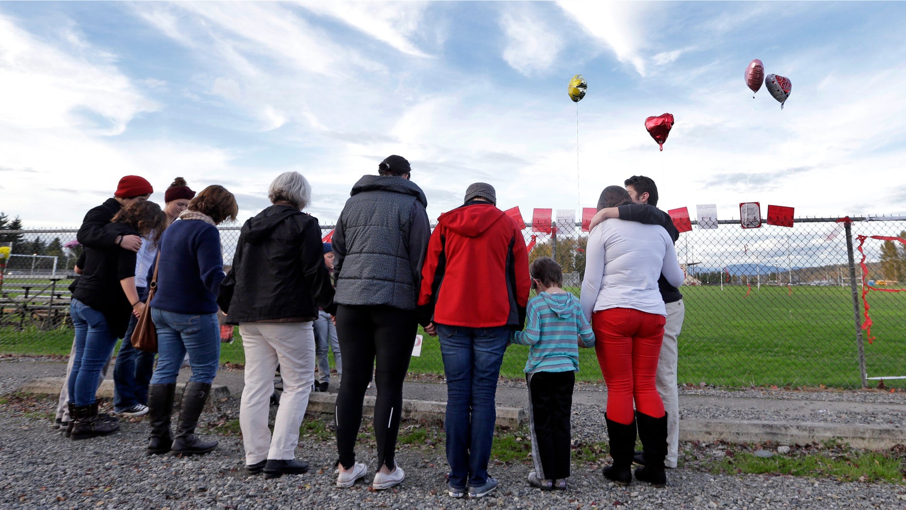 Oct. 29, 2014: People gather in a prayer circle at a fence at Marysville-Pilchuck High School covered with flowers, balloons and messages memorializing a shooting there last week.