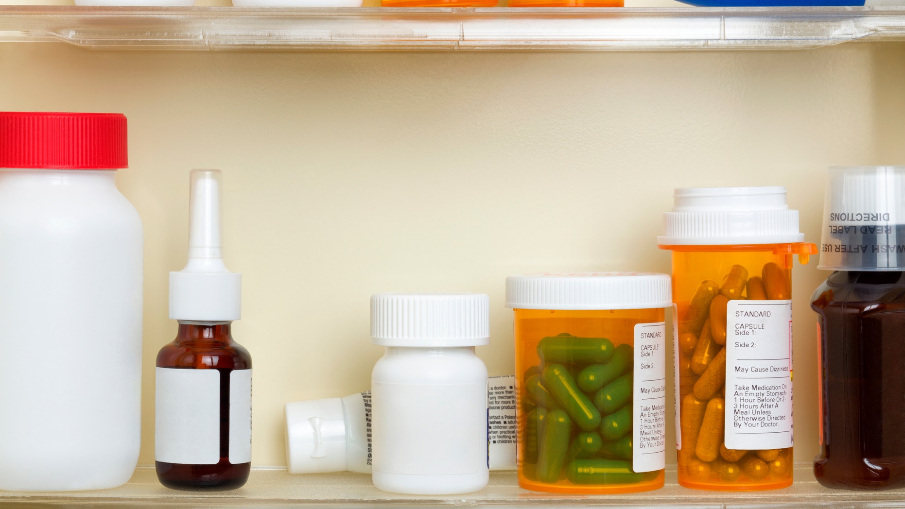 Several containers of over the counter and prescription medications on the shelves of a 1960's medicine cabinet.