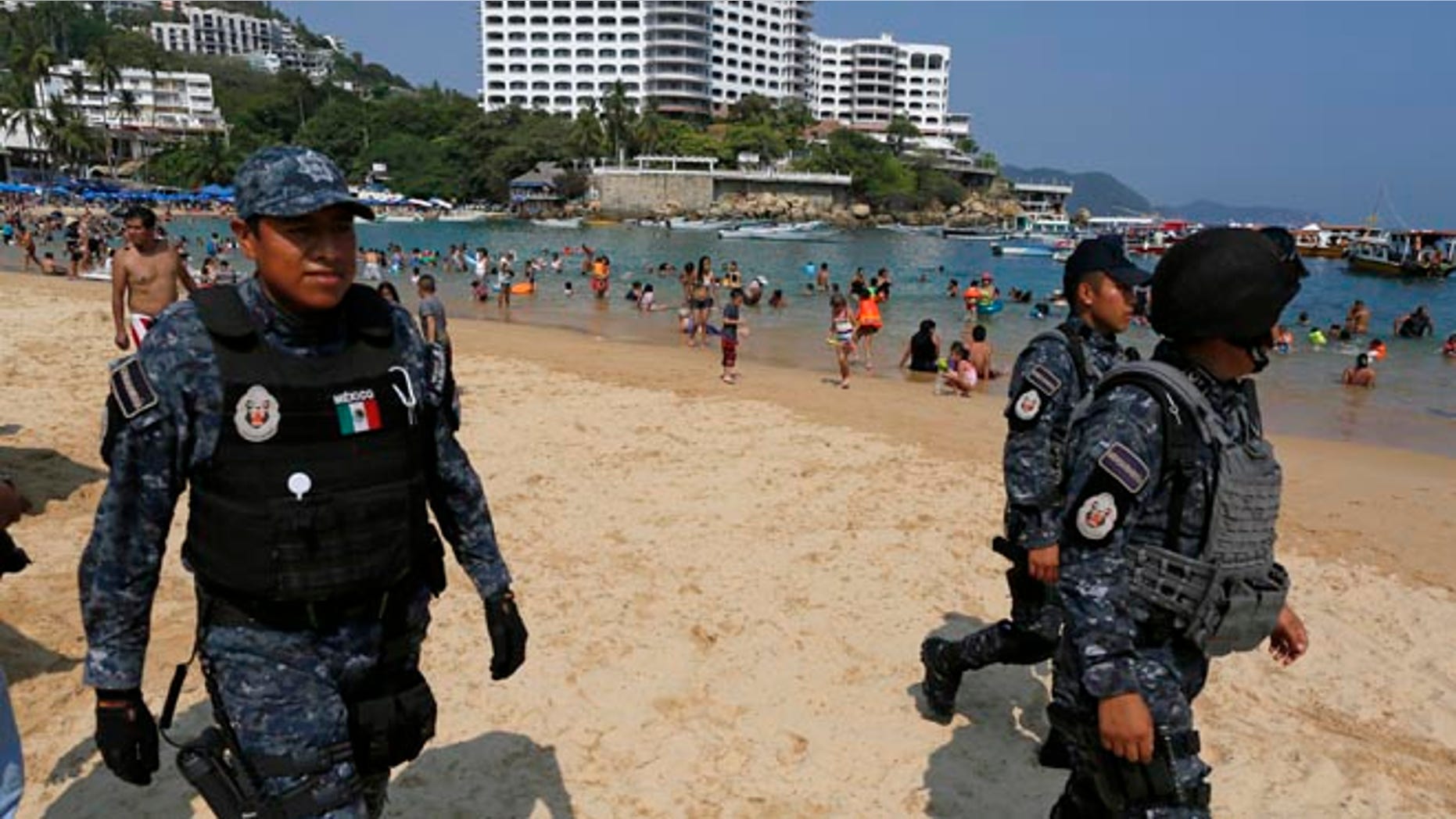 Federal police officer patrol Caleta beach crowded with local residents and tourists in Acapulco, Mexico, Friday, May 13, 2016. The city of Acapulco and Guerrero state in general have experienced a wave of violence attributed to warring drug gangs. On Saturday Mexican authorities say three men were gunned down, in a tourist-hotel quarter of the Pacific resort city. (AP Photo/Enric Marti)