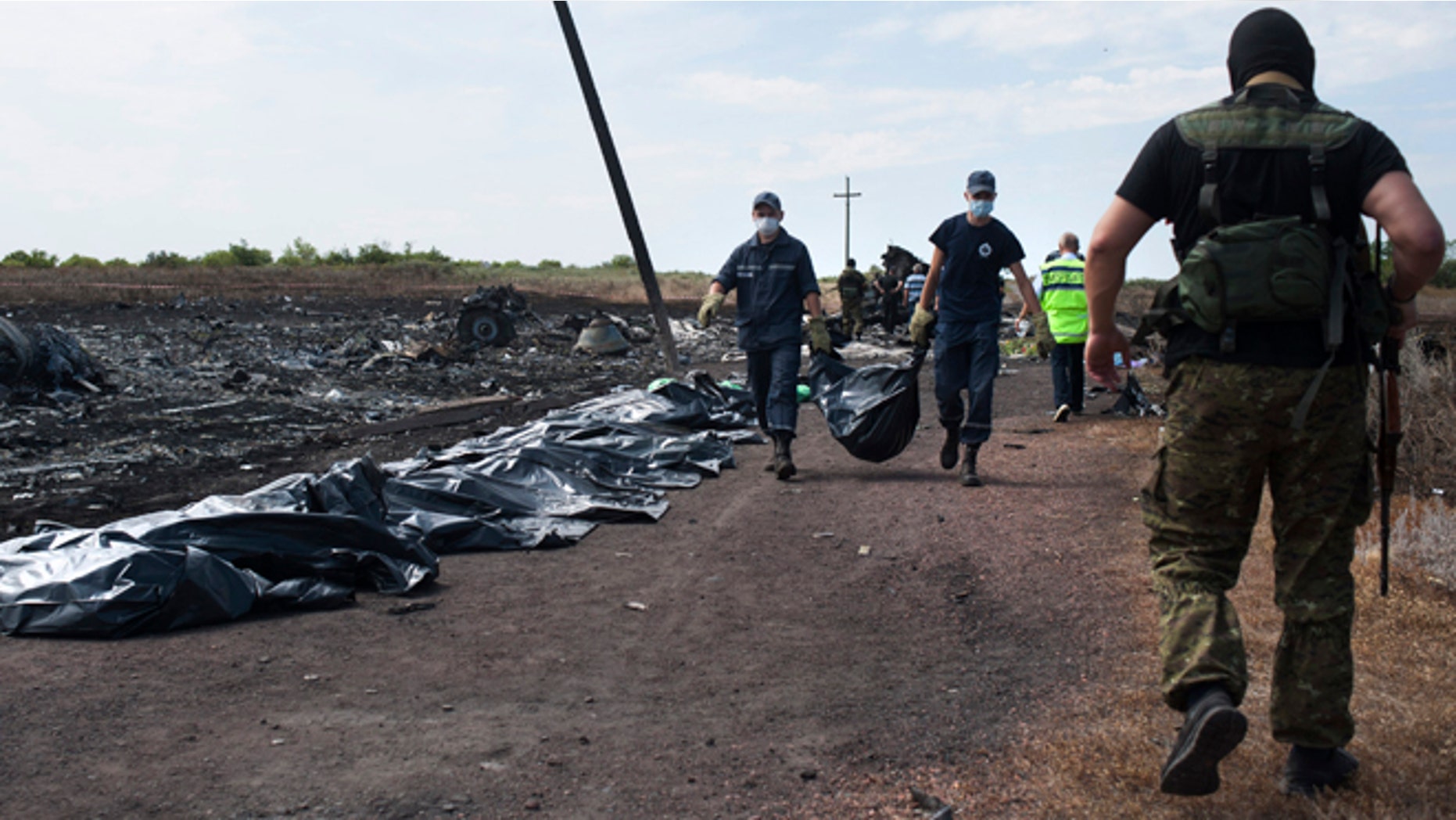 July 20, 2014: Ukrainian emergency workers carry a victim's body in a bag as a pro-Russian fighter, right back to a camera, guards the crash site of Malaysia Airlines Flight 17· near the village of Hrabove, eastern Ukraine.