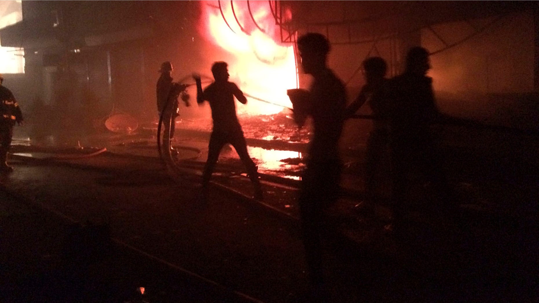 July 3, 2016: Iraqi firefighters extinguish a fire as civilians gather after a car bomb at a commercial area in the Karada neighborhood of Baghdad
