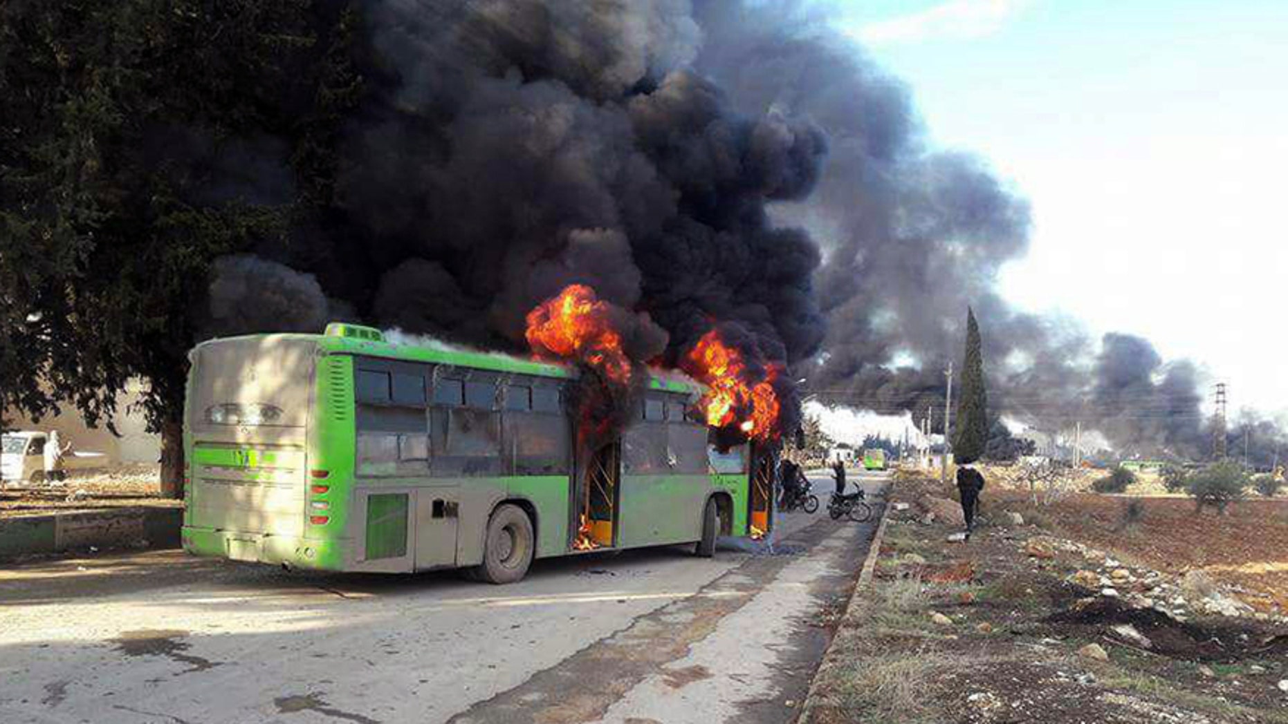In this photo released by the Syrian official news agency SANA, smoke rises in green government buses, in Idlib province, Syria, Sunday, Dec. 18, 2016. Activists said, militants have burned at least five buses assigned to evacuate wounded and sick people from two villages in northern Syria. The incident could scuttle a wider deal that encompasses the evacuation of thousands of trapped rebel fighters and civilians from the last opposition foothold in east Aleppo. (SANA via AP)