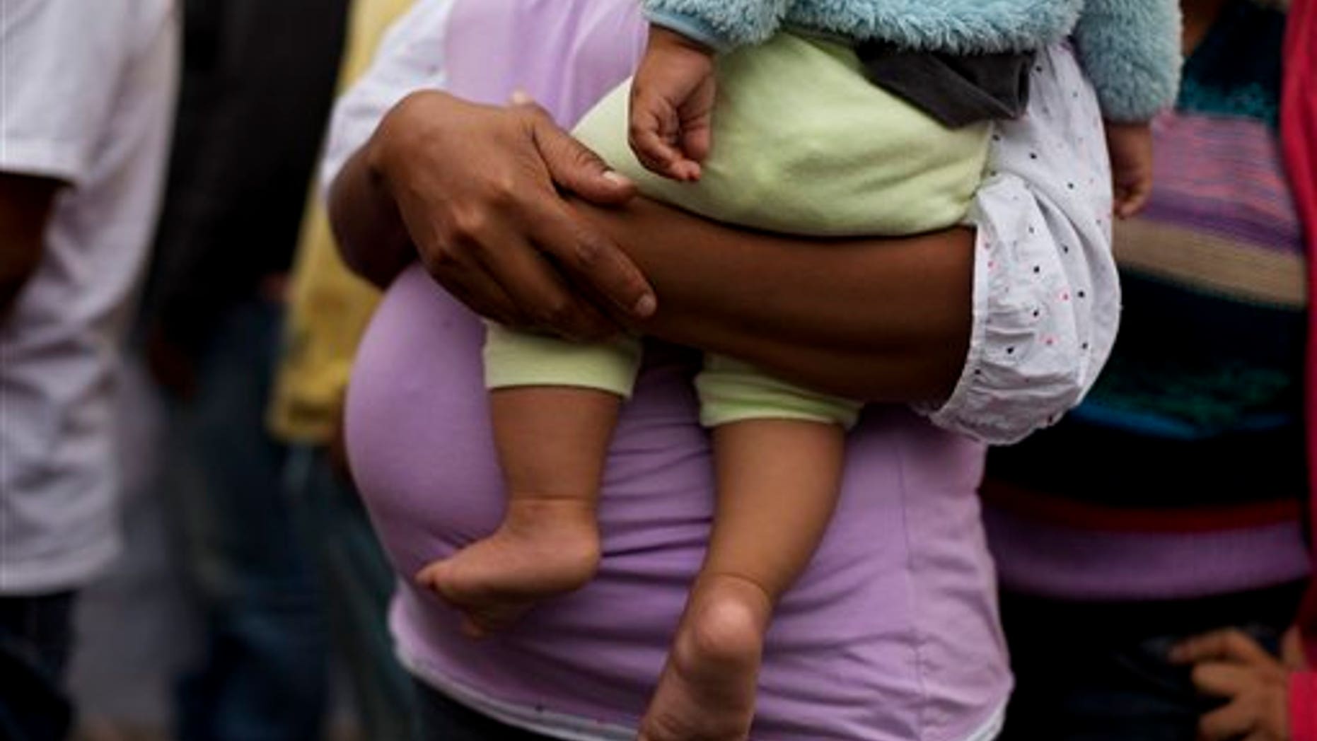 Honduran migrant Velma Flores holds her friend's son Miguel Antonio, 7 months, as she walks with a group of illegal migrants arriving in Mexico City escorted by human rights activists, Tuesday, June 3, 2014. Flores, who is pregnant and traveling with two young daughters, is one of vast numbers of Central American migrants undertaking the risky overland crossing through Mexico. Illegal migrants face abuse from both criminal gangs and Mexican police, but many say the economic or security situation in their home countries leaves them no choice but to try to reach the U.S.(AP Photo/Rebecca Blackwell)