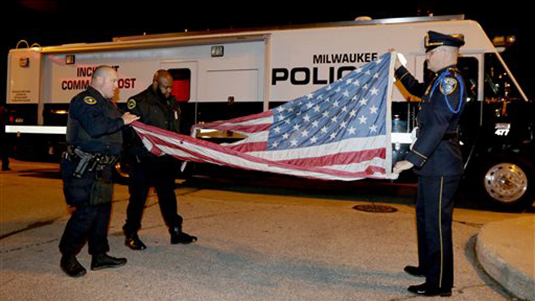 Nov. 10, 2015: In this provided by the Milwaukee Police Department, officers, from left, Jedidiah Thompson, Jutiki X and Joel Rossman fold a flag they recovered after it was set on fire by a protester outside the Republican presidential debate in Milwaukee.