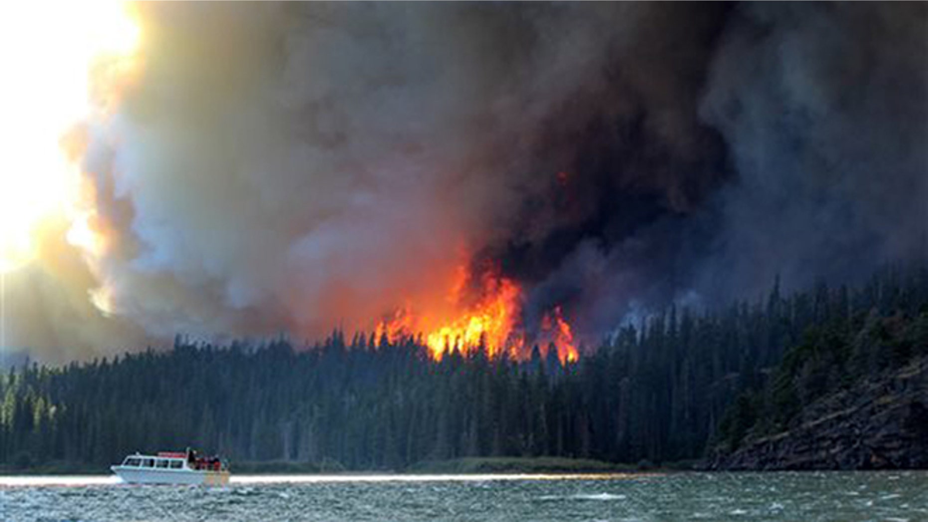 In this photo provided by Erin Conwell, taken Tuesday, July 21, 2015, fire and smoke from the the Reynolds Creek wildfire rises above the landscape at St. Mary Lake in Glacier National Park, Mont.