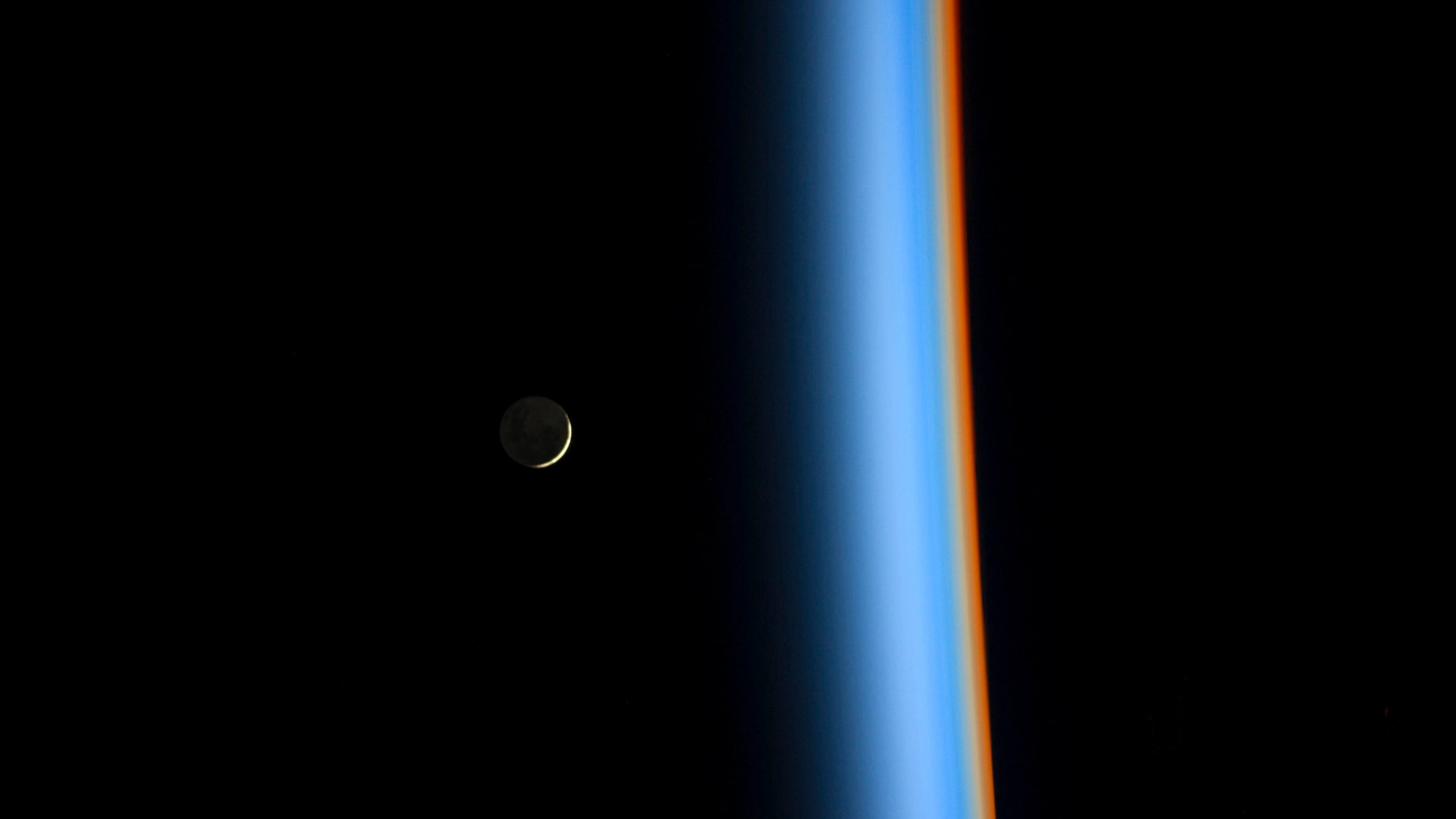 A crescent moon rises over the cusp of the Earth's atmosphere.