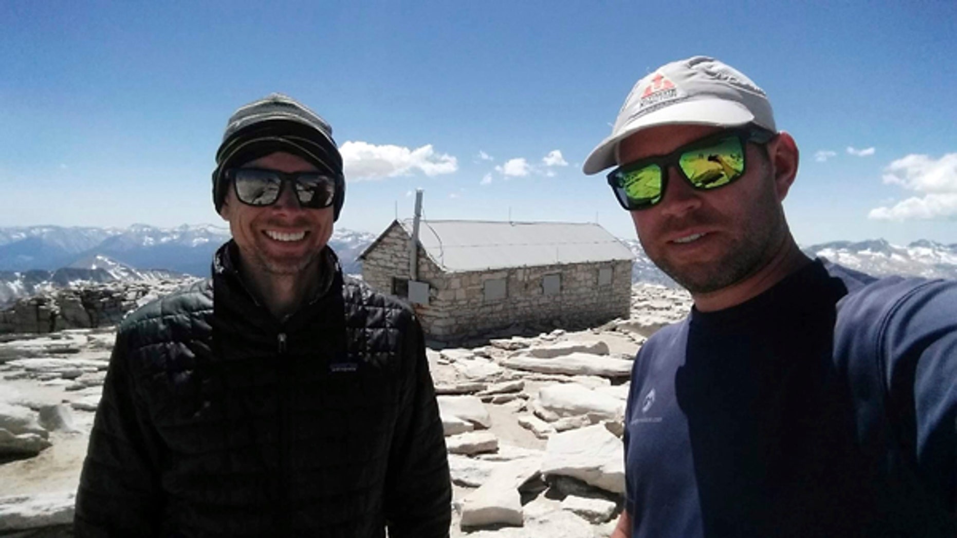 In this August 2017 photo provided by Brian McKinney, Sam Vonderheide, right, and McKinney, left, pose for a photo on the top of Mount Whitney, Calif. The two hikers walking a High Sierra trail videotaped a nerve-wracking stare-down with a wild mountain lion on July 23. The video shows the adult lion scurry down a winding trail out of sight; moments later the hikers round a turn to see the large cat peering down on them from a rocky perch feet away. (Brian McKinney via AP)
