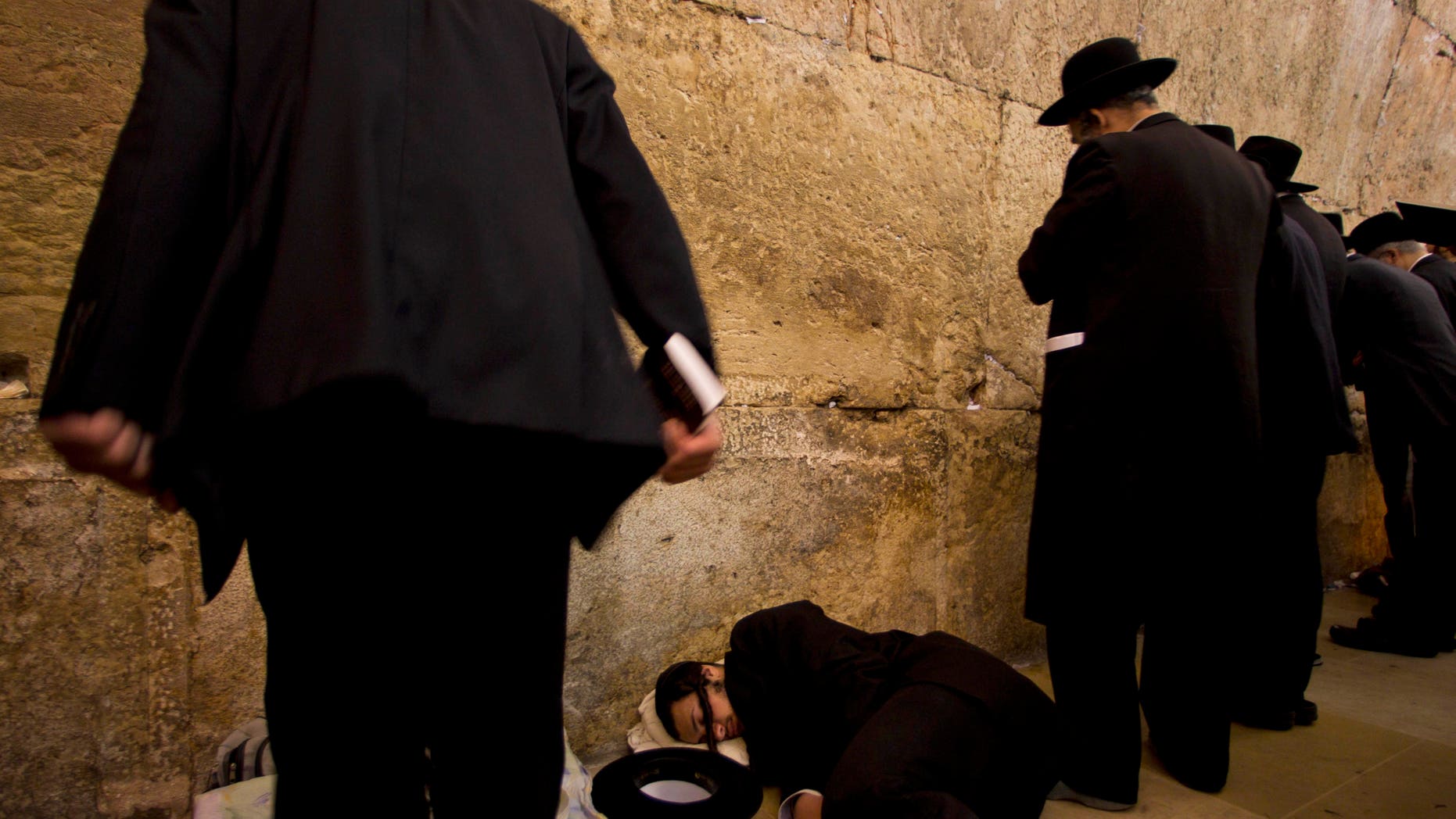 An Ultra-orthodox Jewish man sleeps as others pray during the mourning ritual of Tisha B'Av at the Western Wall, the holiest site where Jews can pray, in Jerusalem's Old City, Tuesday, Aug. 9, 2011. The Jewish holy day of Tisha B'Av, when Jews mourn the destruction of the biblical temples, is marked Tuesday. (AP Photo/Bernat Armangue)