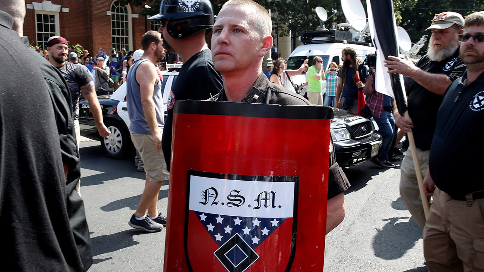 A white supremacist holds a shield with National Socialist Movement symbols on it as he arrives at a rally in Charlottesville, Va., Aug. 12, 2017.