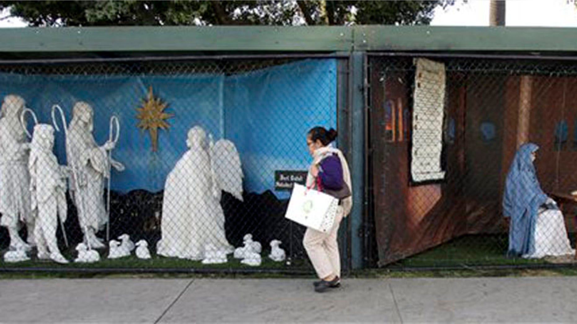 FILE - In this Dec. 13, 2011 file photo, a woman walks past a two of the traditional displays showing the Nativity scene along Ocean Avenue at Palisades Park in Santa Monica, Calif.