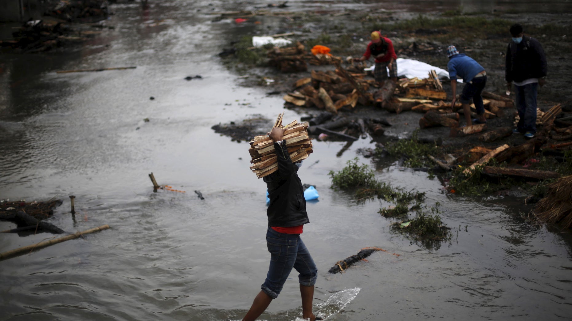 A man carries wood for pyre to burn the bodies of victims of Saturday's earthquake, during the cremation along a river in Kathmandu, Nepal April 28, 2015. REUTERS/Adnan Abidi - RTX1AOND