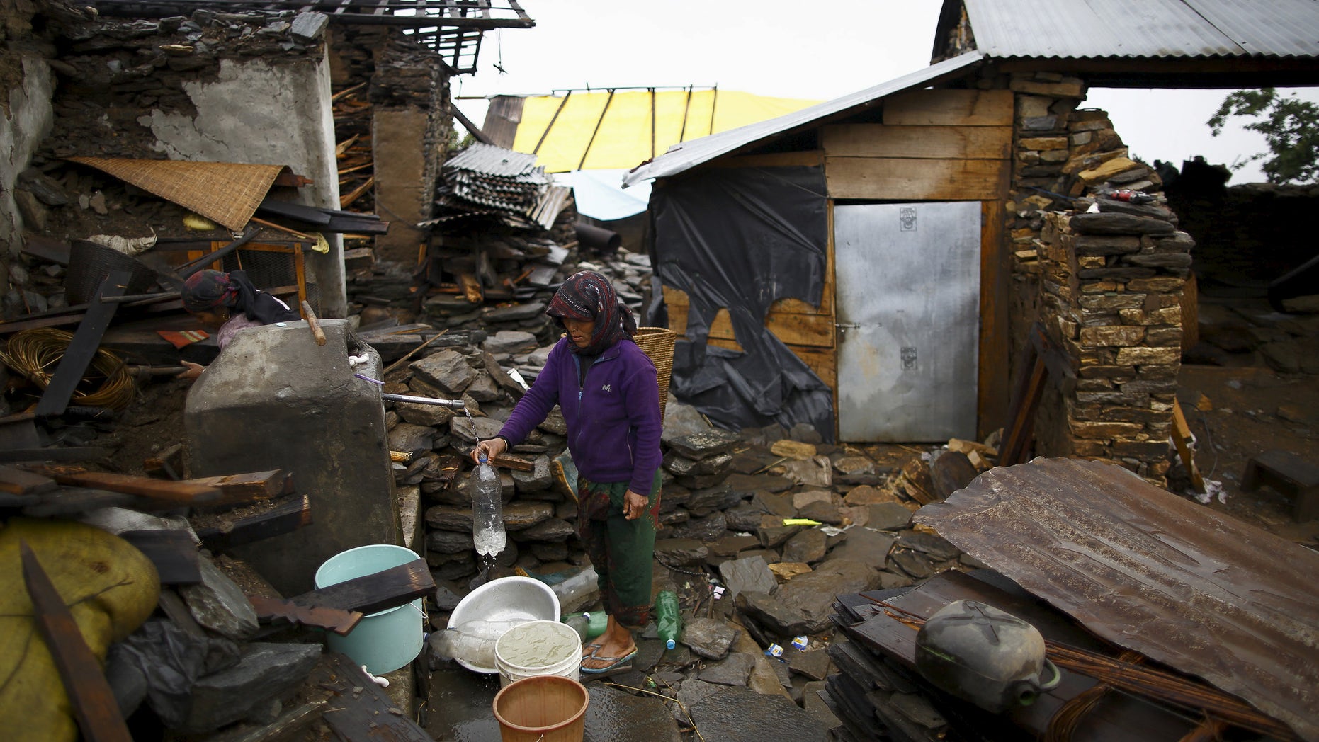 An earthquake victim fills water from a tap near the debris of a collapsed house at Barpak village at the epicenter of the April 25 earthquake in Gorkha district, Nepal, May 21, 2015. REUTERS/Navesh Chitrakar