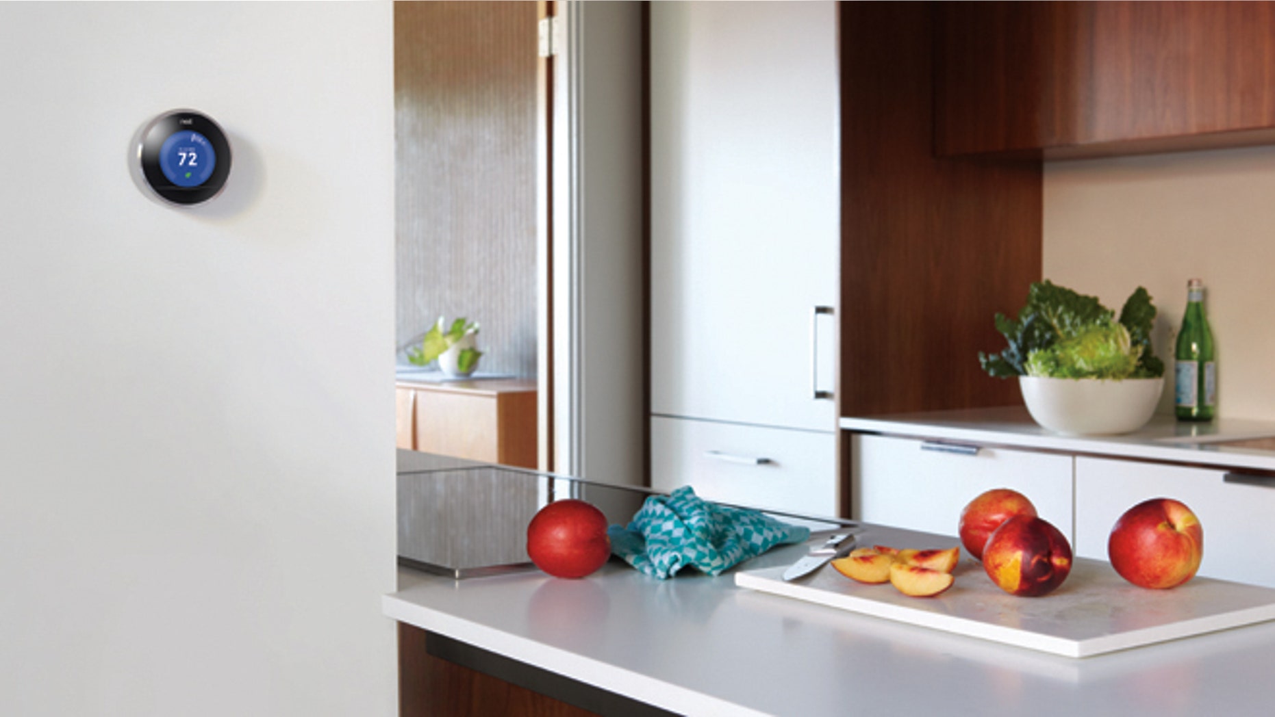 A Nest smart thermostat is seen on the wall of a kitchen.