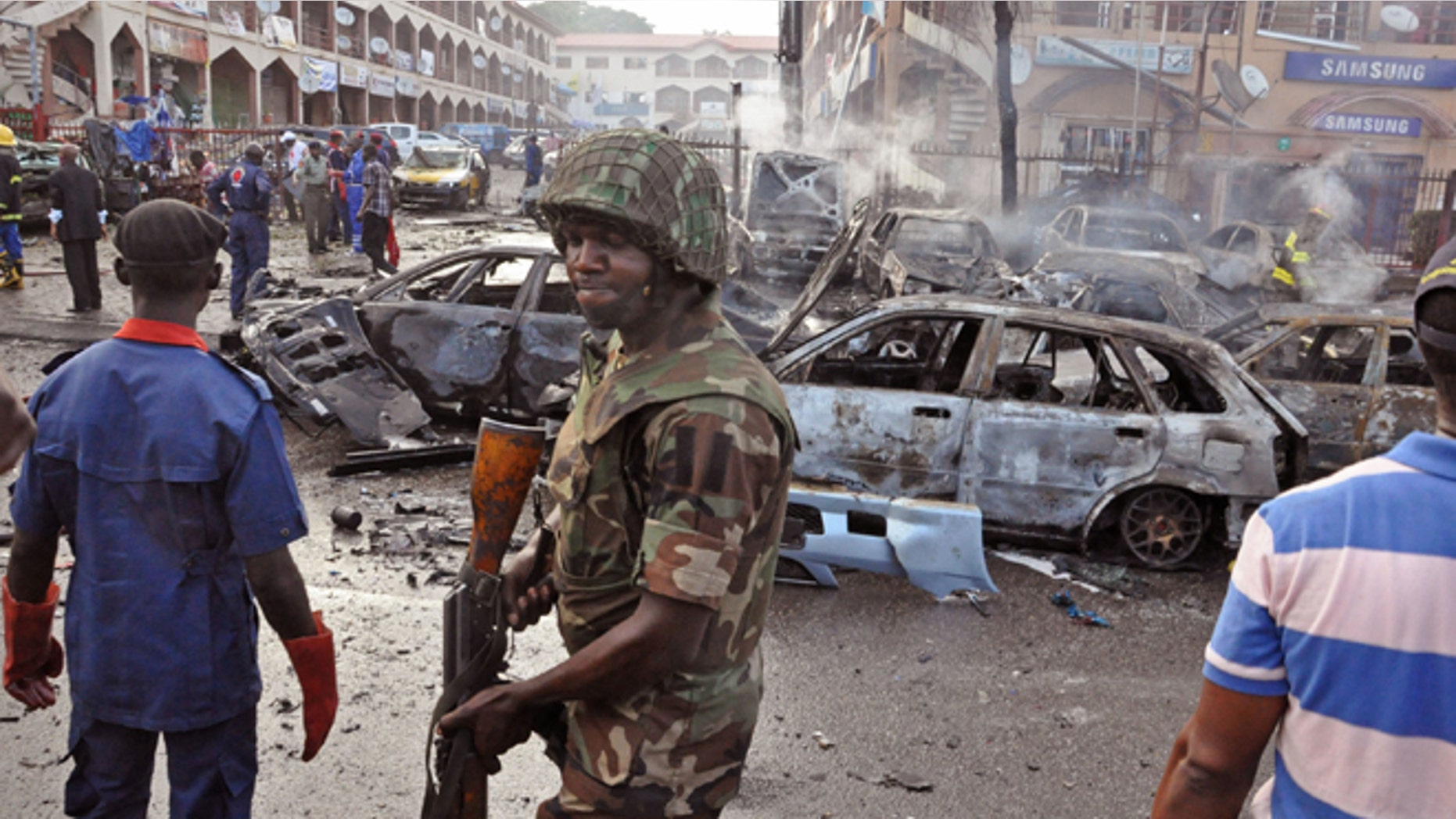 June, 25, 2014: In this file photo, a Nigerian soldier, center, walks, at the scene of an explosion in Abuja, Nigeria. A car bomb exploded in a market in Nigeria's northeastern city of Maiduguri on Tuesday morning, July 1, 2014 and dozens of people are feared dead, witnesses said.