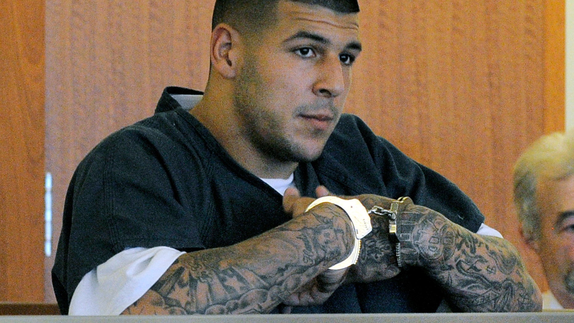FILE - In this June 27, 2013 file photo, former New England Patriots football standout Aaron Hernandez stands during a bail hearing in Superior Court in Fall River, Mass., charged with killing Odin Lloyd. Hernandez is scheduled to be arraigned May 28, 2014, on two unrelated murder charges in the 2012 shooting deaths of Daniel de Abreu and Safiro Furtado in Boston. Prosecutors are also seeking assistance from tattoo artists who may have inked Hernandez's right arm between February 2012 and June 2013. The tattoo artists are considered witnesses, not suspects. (AP Photo/Boston Herald, Ted Fitzgerald, Pool, File)